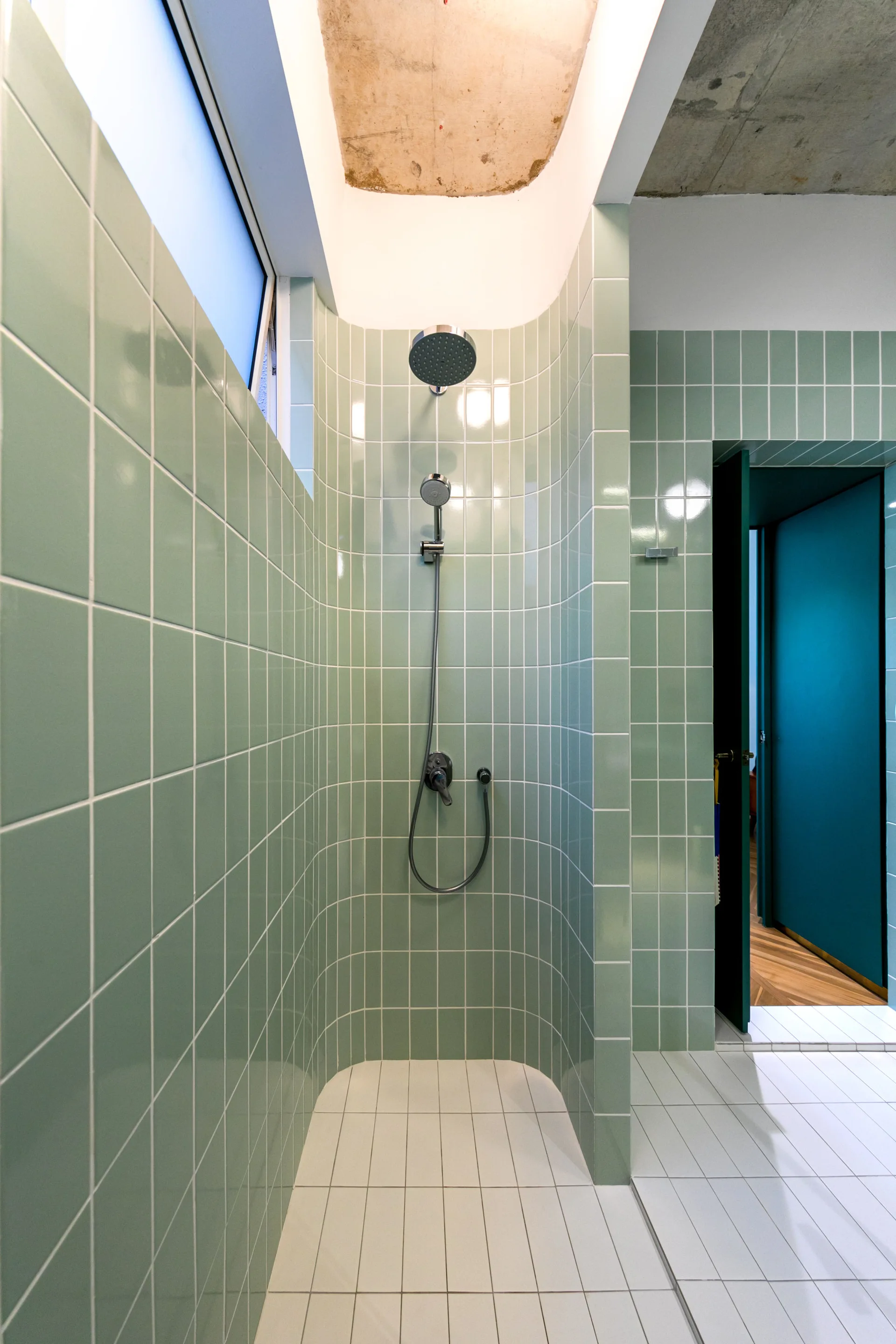 A walk-in shower features curved walls clad in glossy sage green grid tiles, white tiled flooring, and chrome fixtures.