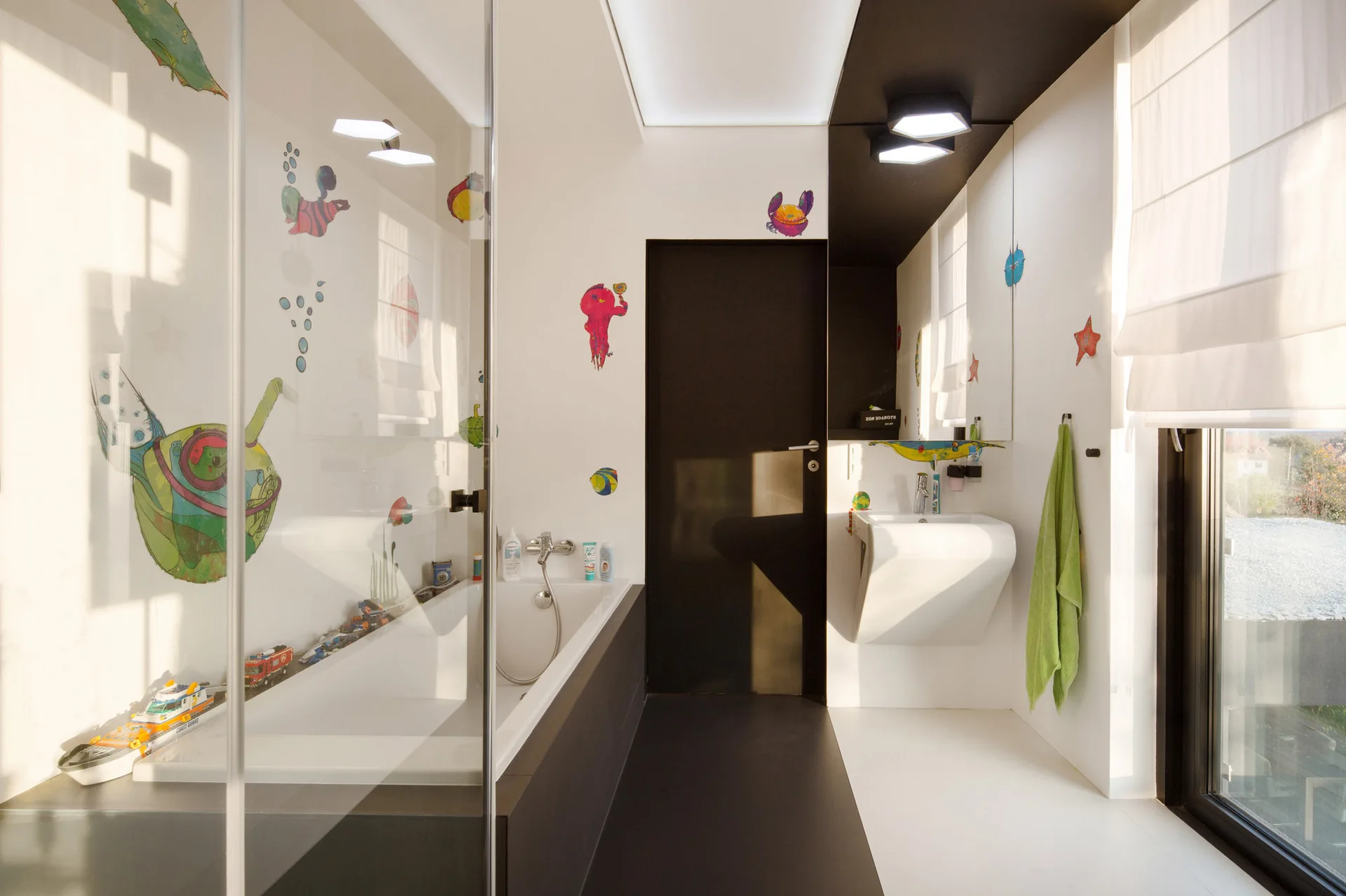 A modern bathroom featuring a white bathtub, a wall-mounted white sink, and whimsical colorful sea creature decals on the white walls.