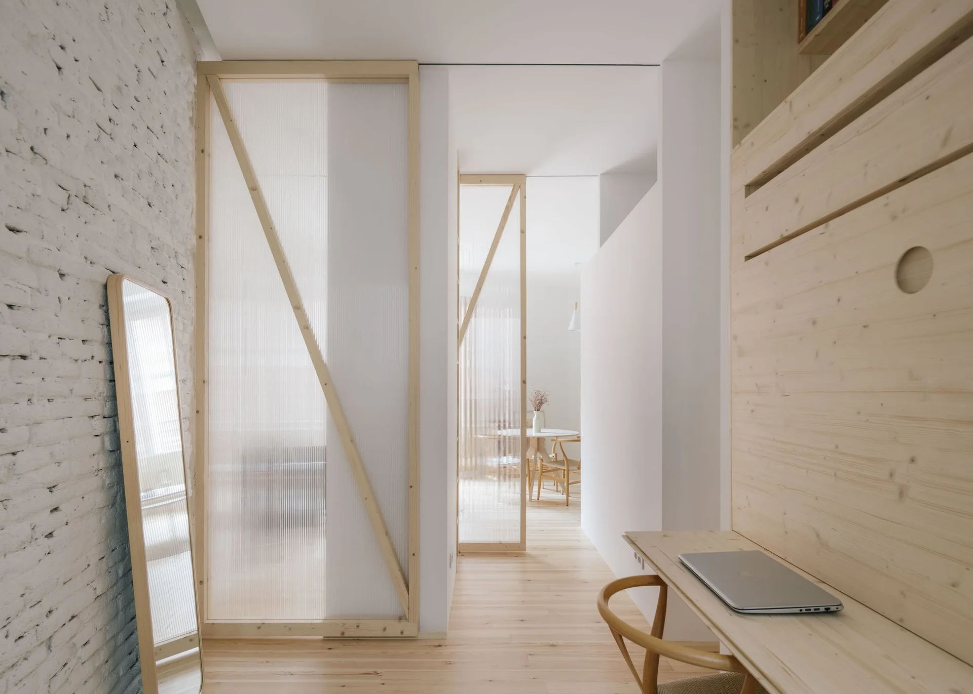 A minimalist hallway featuring fluted glass room dividers with wooden frames, a white brick wall, and a built-in wooden desk.