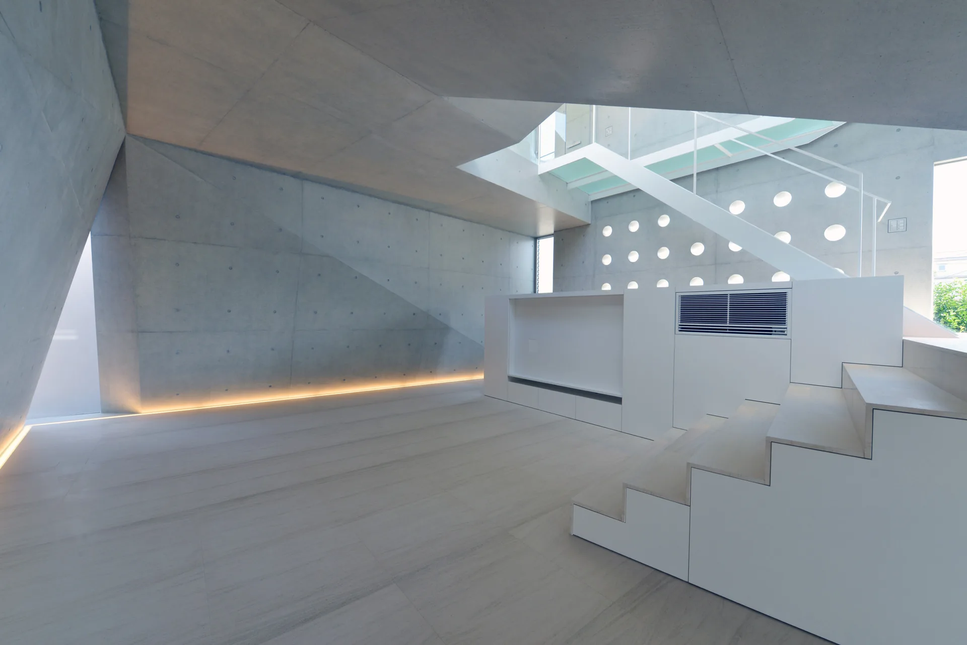A minimalist grey concrete room features a white integrated staircase with built-in cabinets, circular wall cutouts, and low strip lighting along the floor.