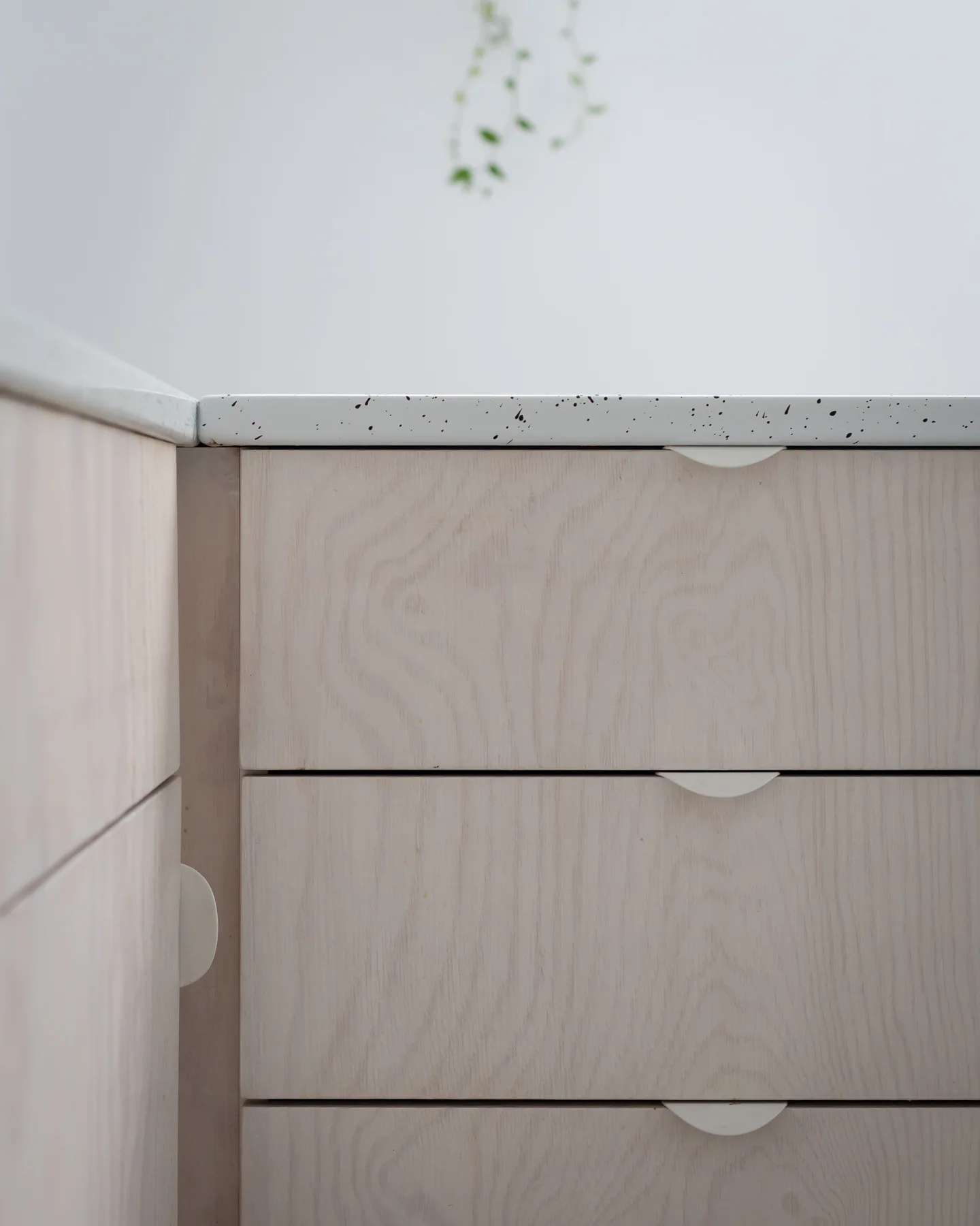 A close-up of light wood drawers featuring white semi-circular pulls beneath a white speckled countertop.