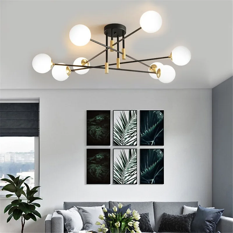 A modern living room features a multi-globe black and gold chandelier hanging above a grey sofa and a grid of six botanical framed art prints.