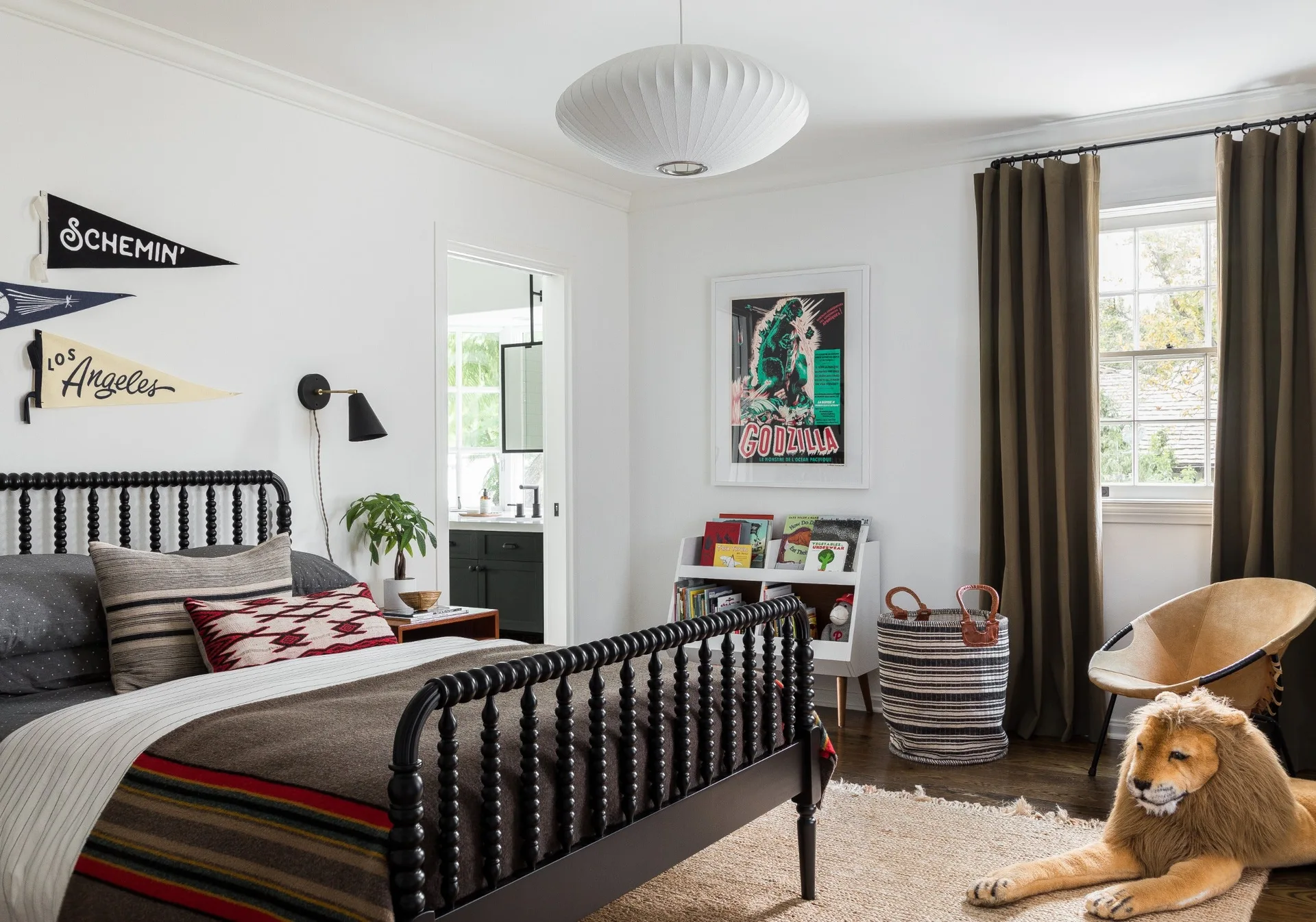 A bedroom features a black spindle bed frame, white walls decorated with pennants, a framed poster, and long olive green curtains.