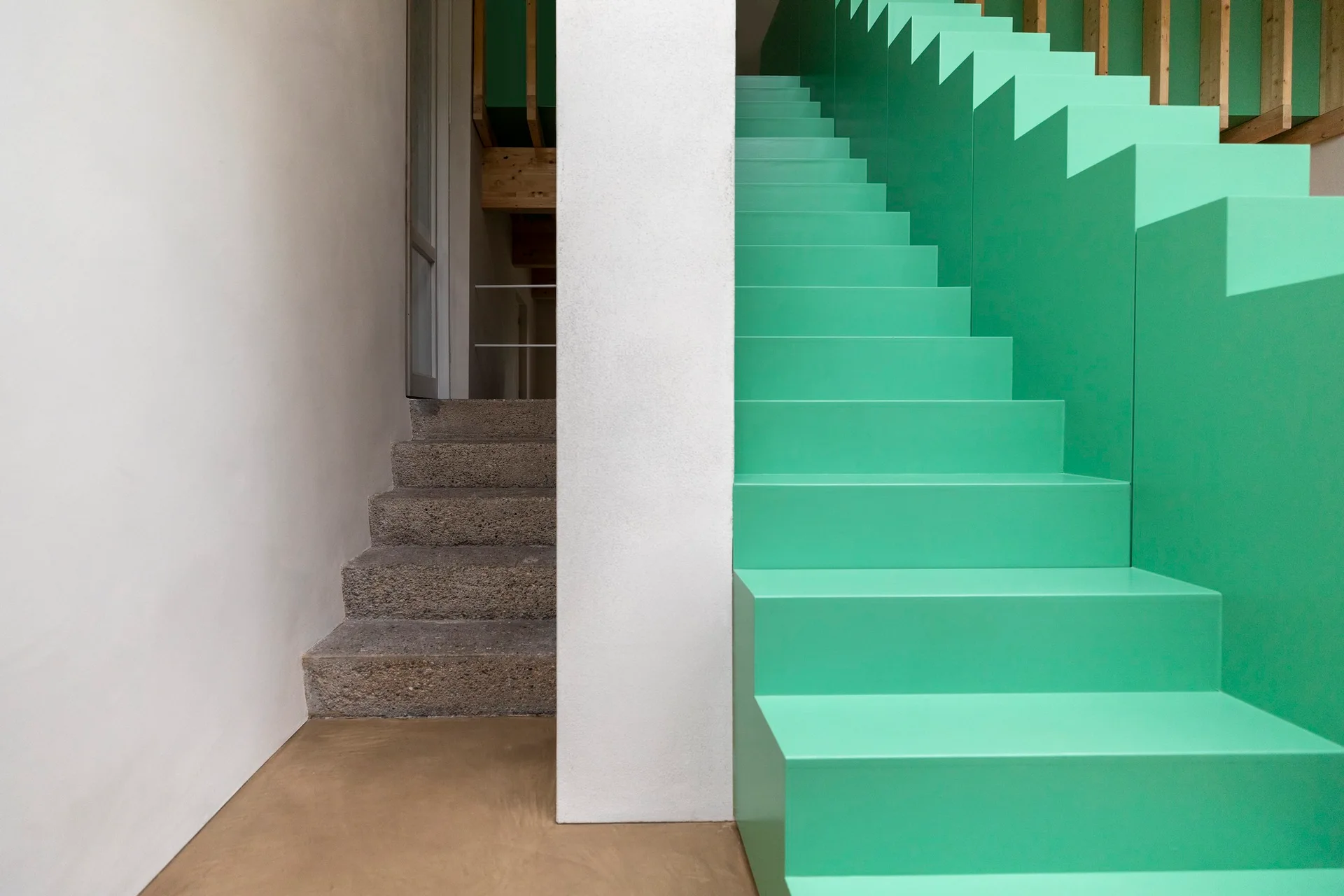 An interior view showing a modern bright green painted staircase side-by-side with a rustic textured stone staircase separated by a white wall.
