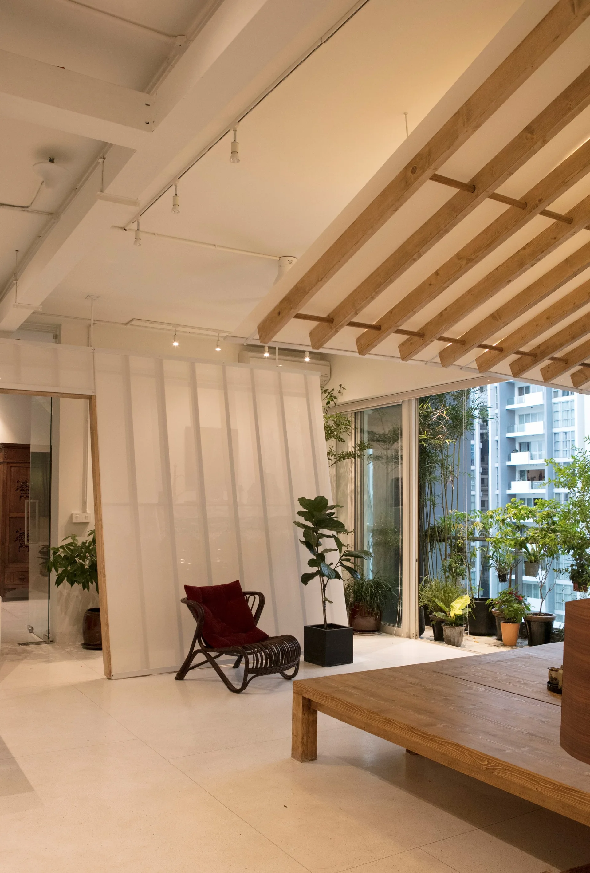A minimalist living space features a slatted wood ceiling, a translucent partition screen, a rattan armchair, and sliding glass doors to a balcony.