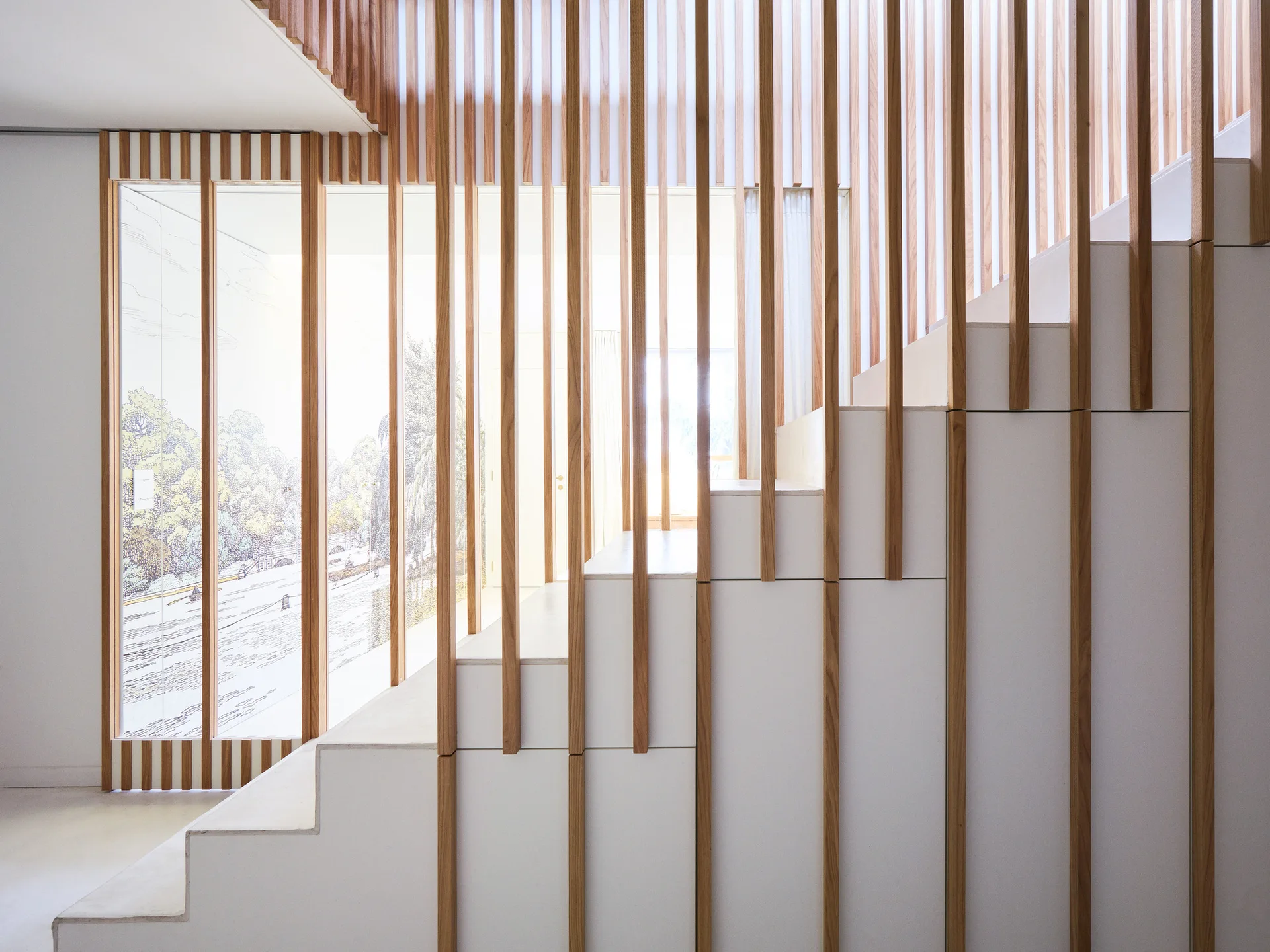 A minimalist white staircase features a vertical light wood slat railing set against a large window with illustrated graphic film.