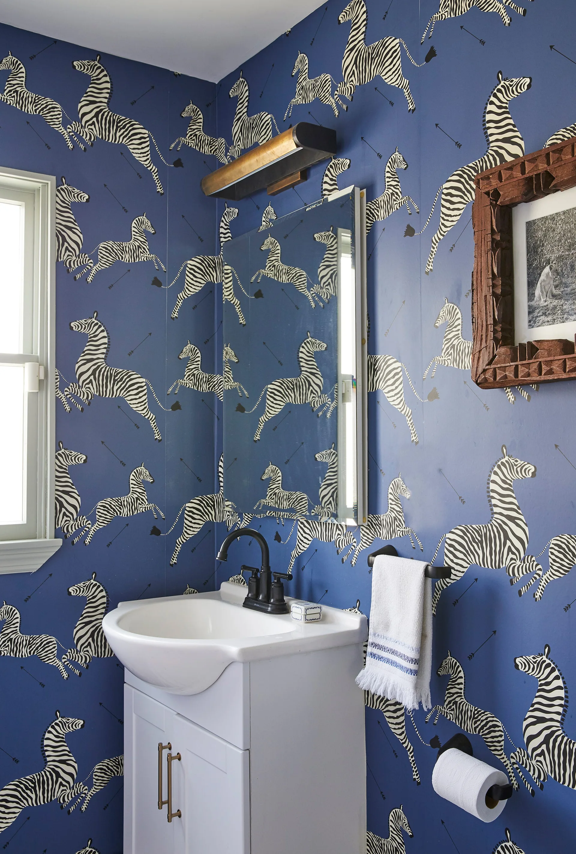 A powder room features bold blue zebra print wallpaper, a white vanity sink, a rectangular mirror, and dark metal fixtures.