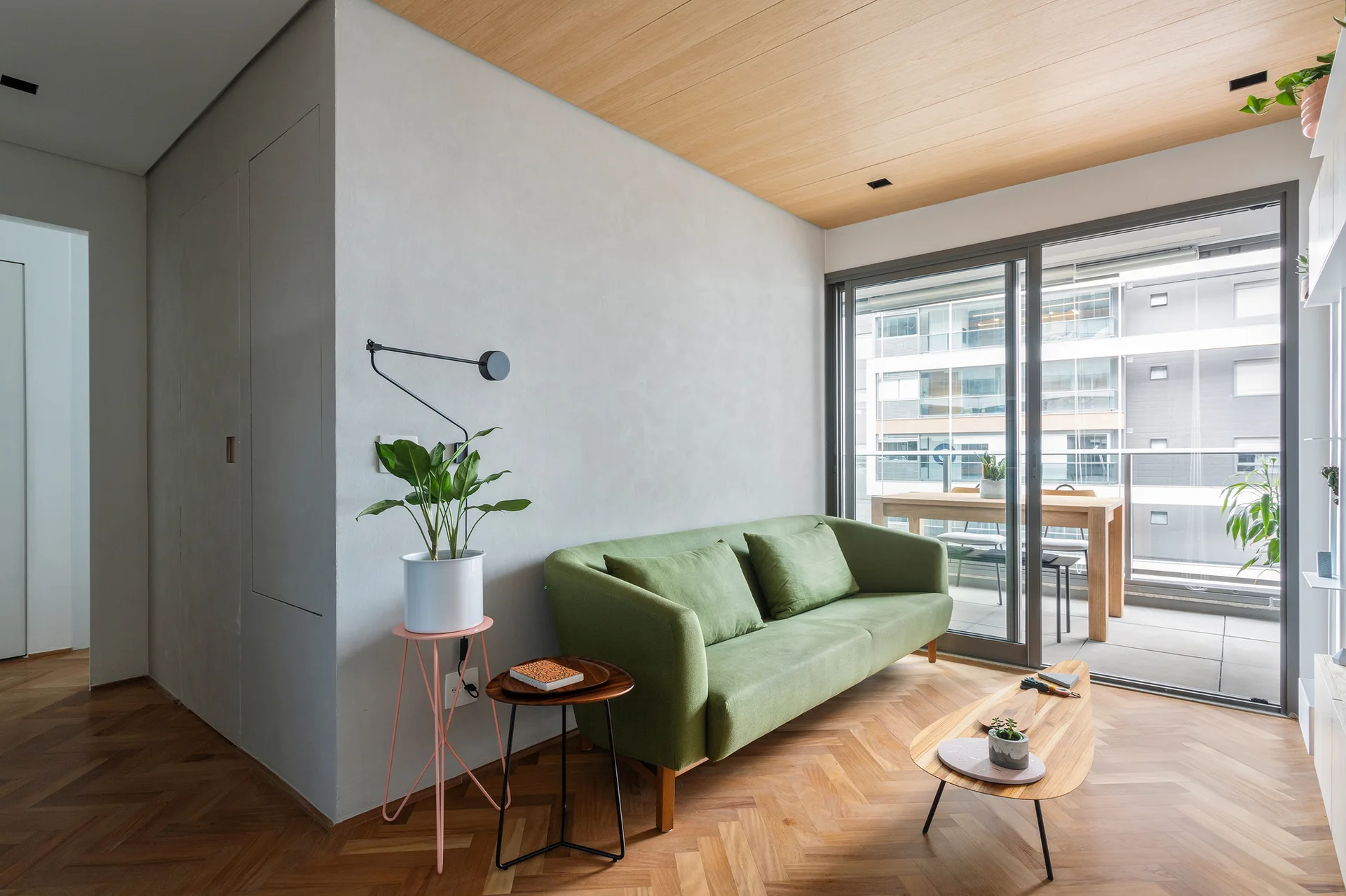 A modern living room with a green sofa on a herringbone wood floor next to sliding glass doors and a wood-paneled ceiling.