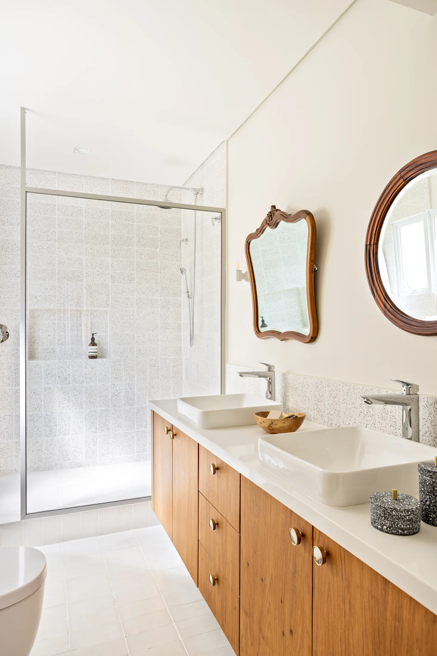 A bright bathroom features a floating wood double vanity with two rectangular vessel sinks, matching chrome faucets, and two vintage wooden mirrors.