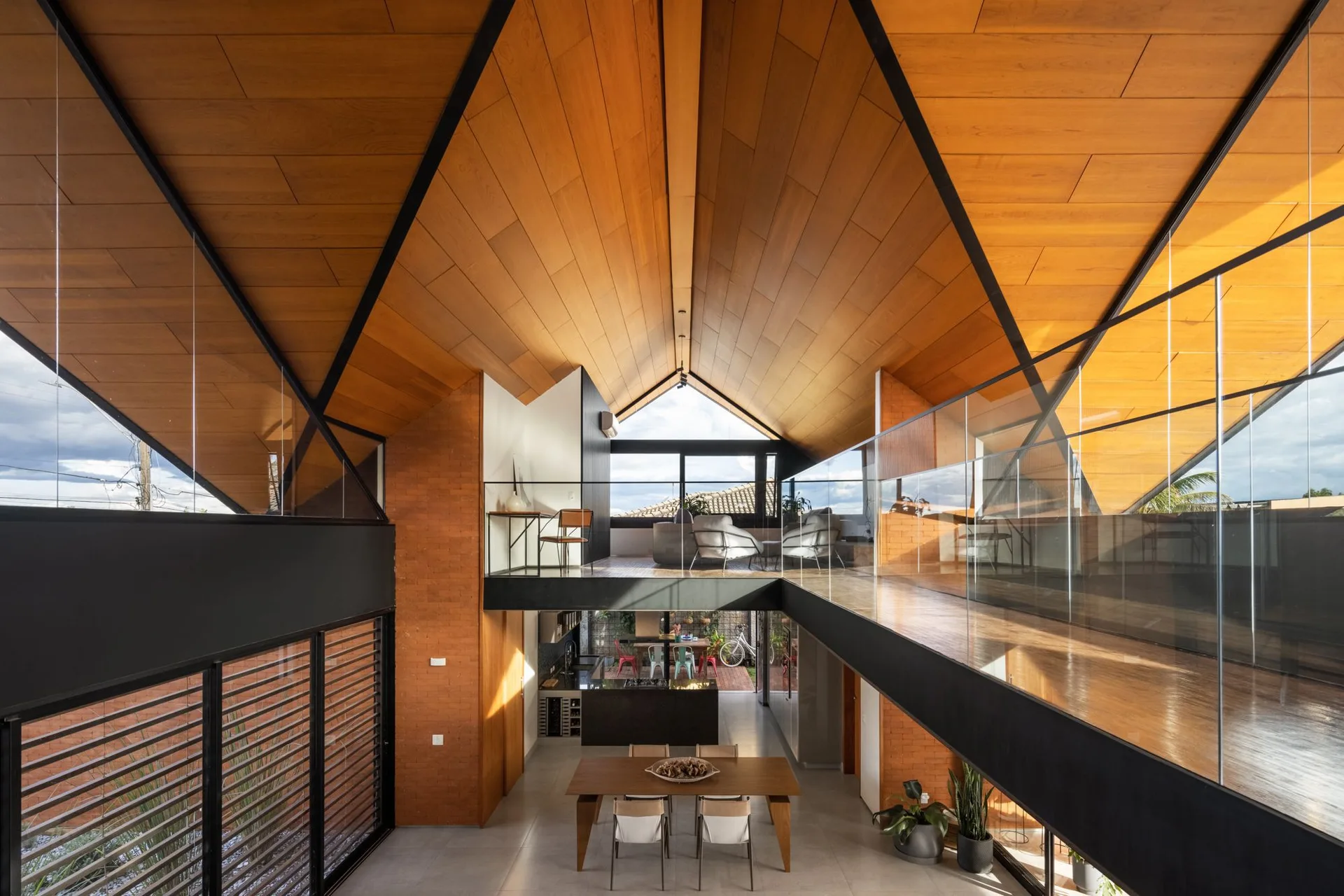A double-height modern home interior features a vaulted wood-paneled ceiling, a mezzanine level with glass railings, and a ground-floor dining area.