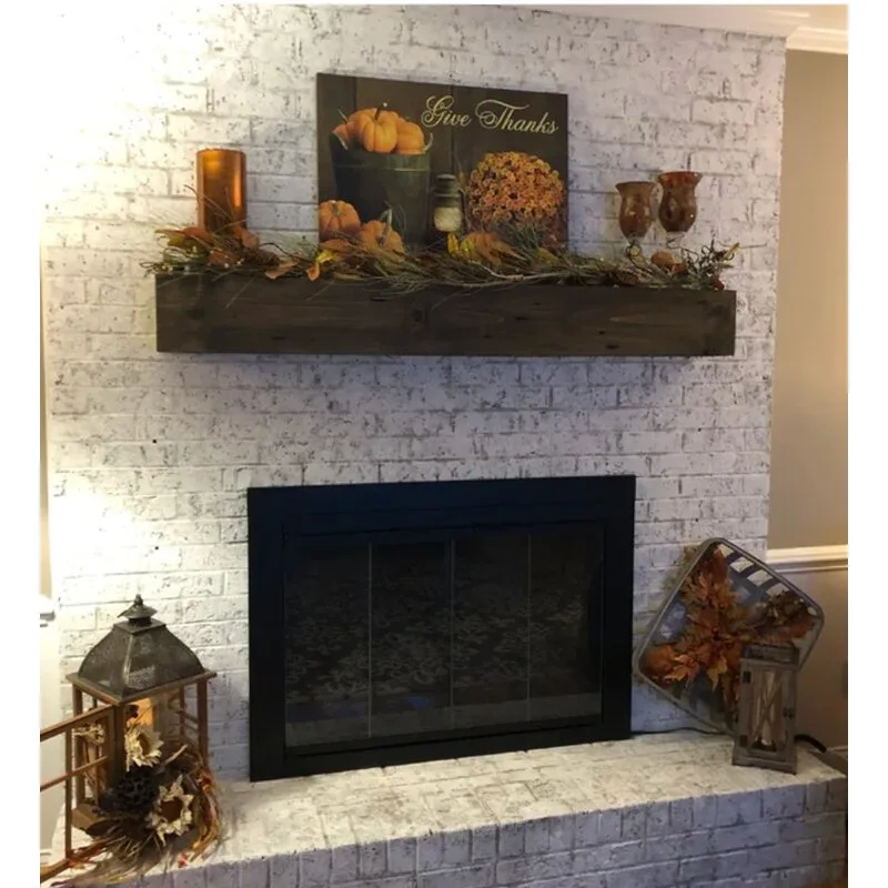 A whitewashed brick fireplace features a dark wood floating mantel styled with autumn garland, lanterns on the hearth, and a black glass insert.