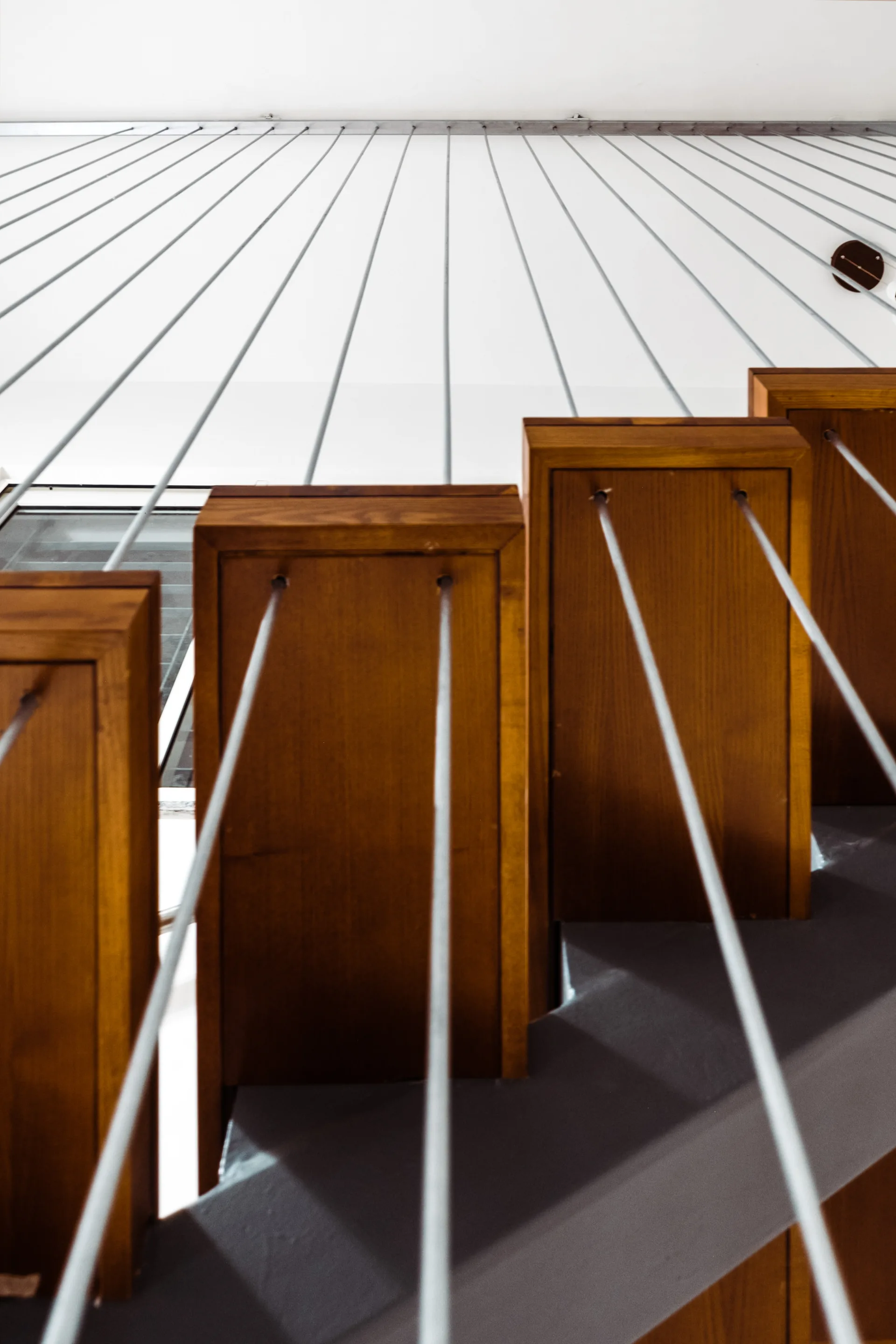 An upward view of wooden stair treads integrated with a minimalist vertical metal cable railing system against a plain white wall.