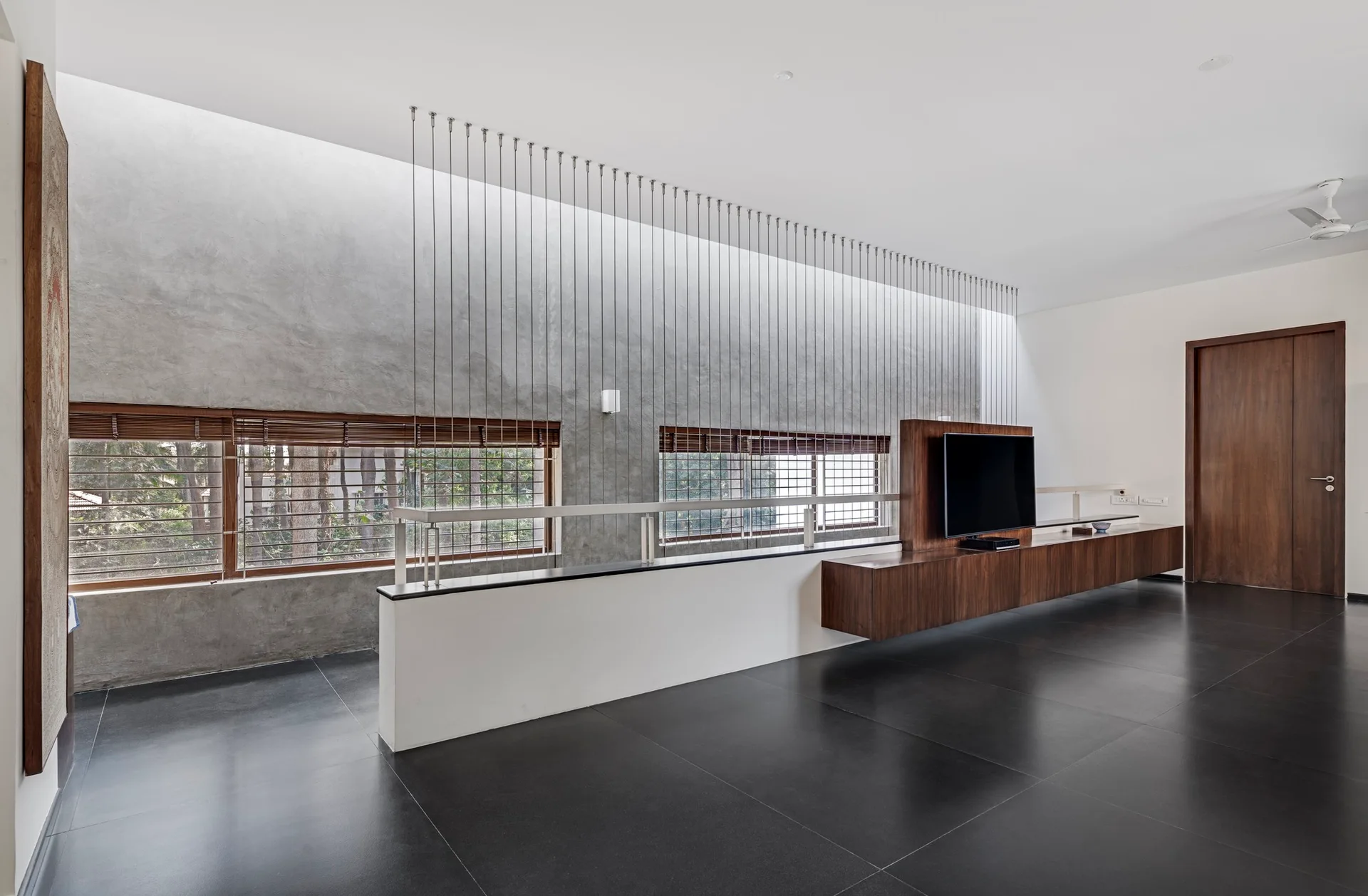 A modern living space features a gray concrete accent wall, a long floating wood media console, and a vertical cable railing room divider.