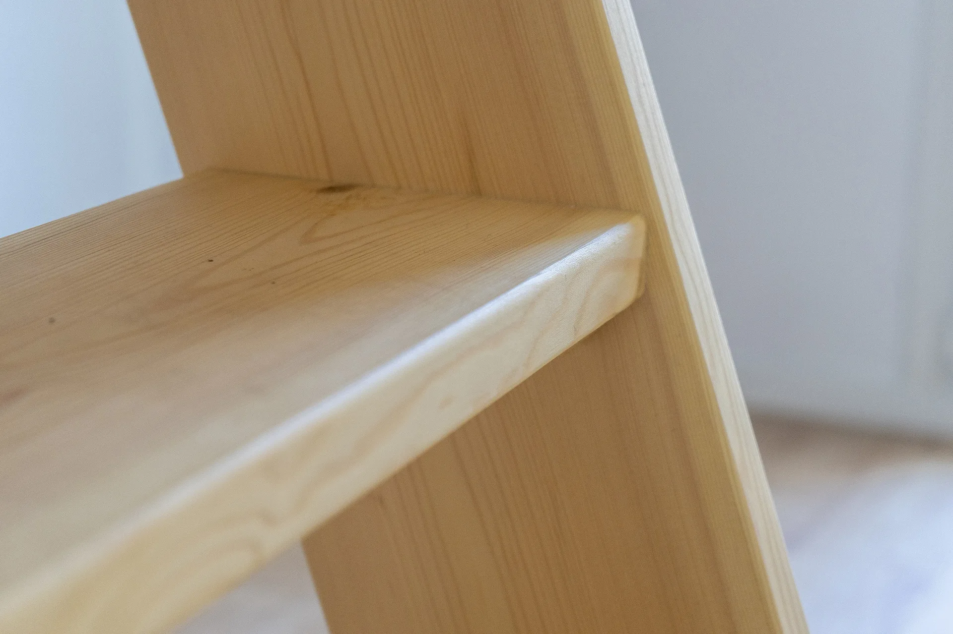 A close-up photograph of a light-toned natural wood shelf with rounded edges and visible wood grain patterns under soft lighting.