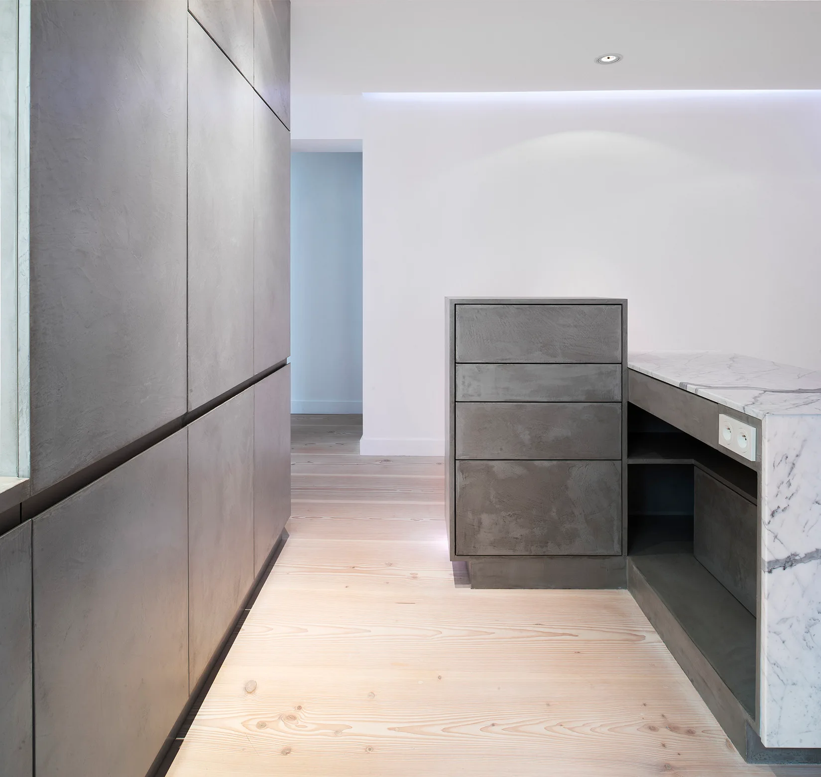 Minimalist gray cabinetry and a matching island with a white marble countertop stand on wide-plank light wood floors.