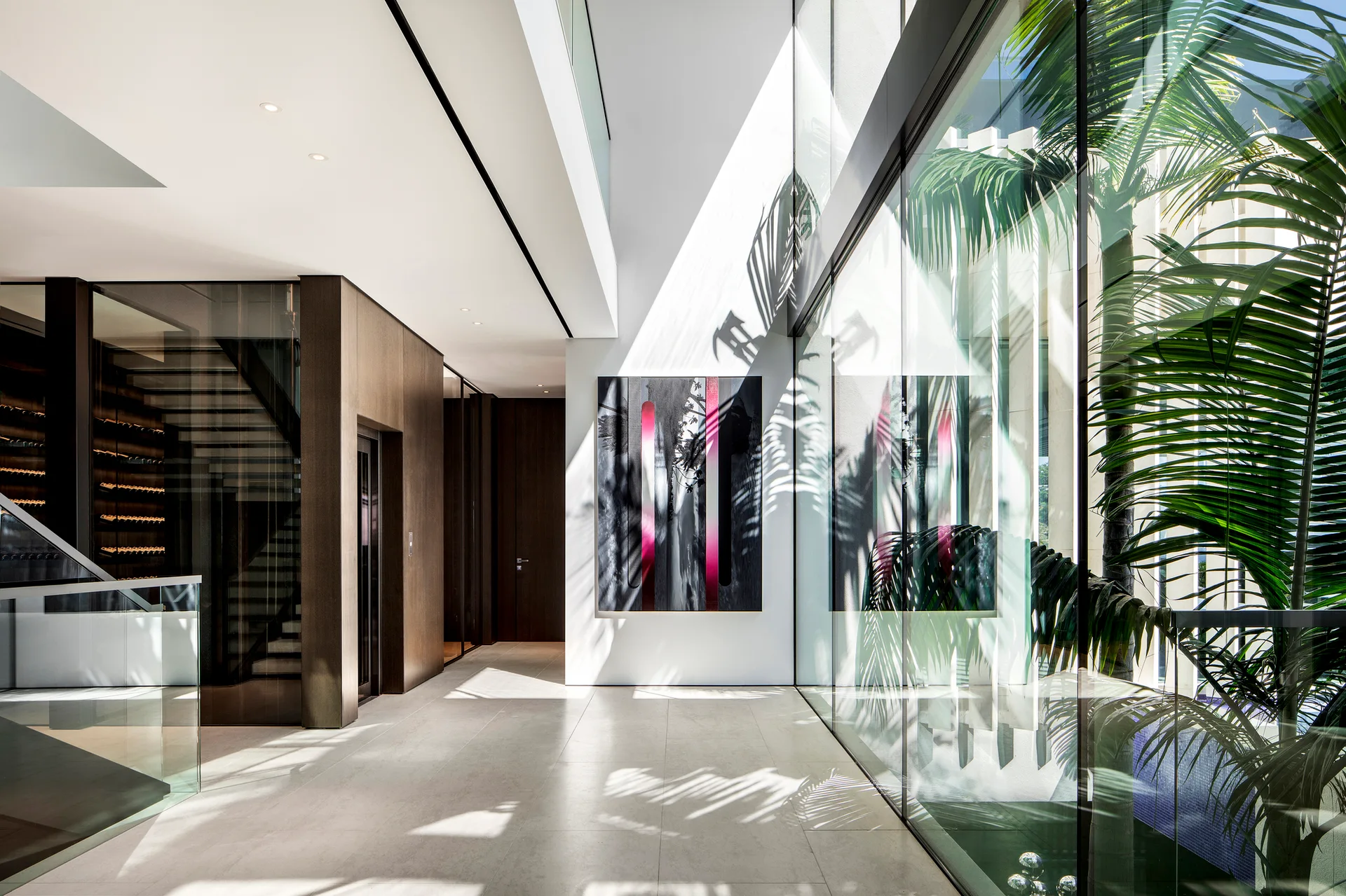 A contemporary minimalist hallway with a large floor-to-ceiling glass wall, light stone floor tiles, and a dark abstract painting on the wall.