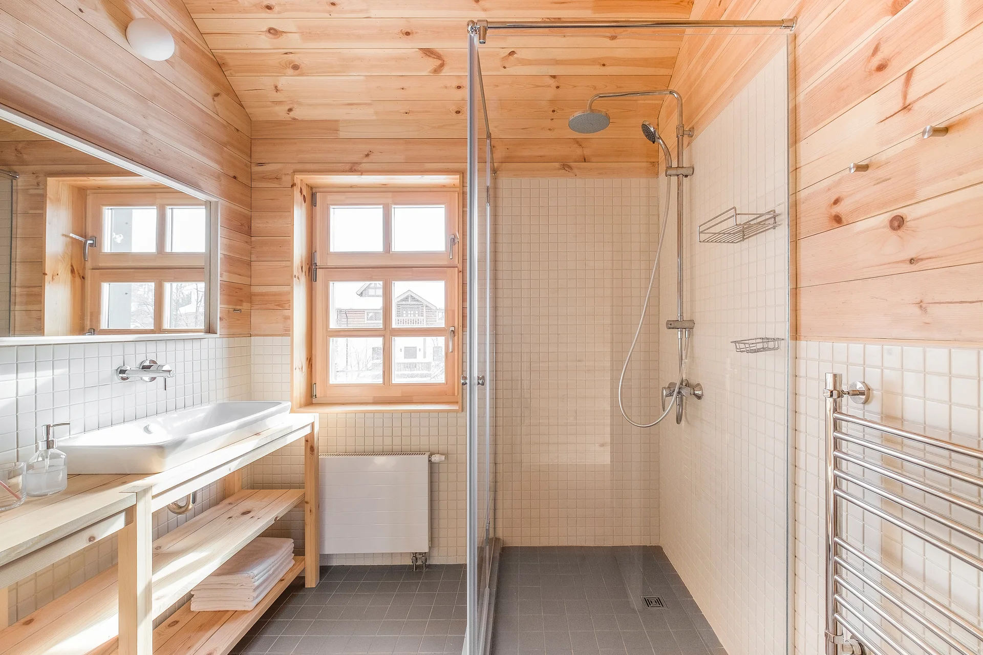 A Scandinavian bathroom features light wood plank walls and ceiling, a glass walk-in shower with white grid tiles, and an open wood vanity.