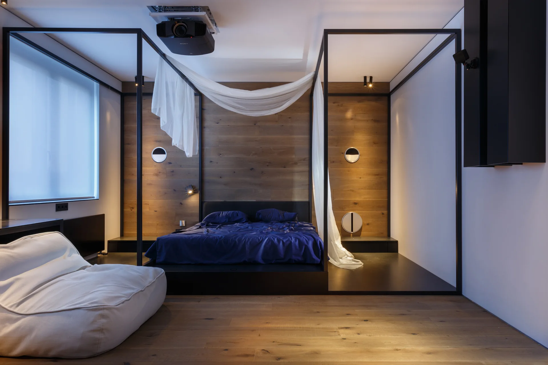 A modern bedroom features a black metal canopy bed set on a dark raised platform against a horizontal wood paneled accent wall.