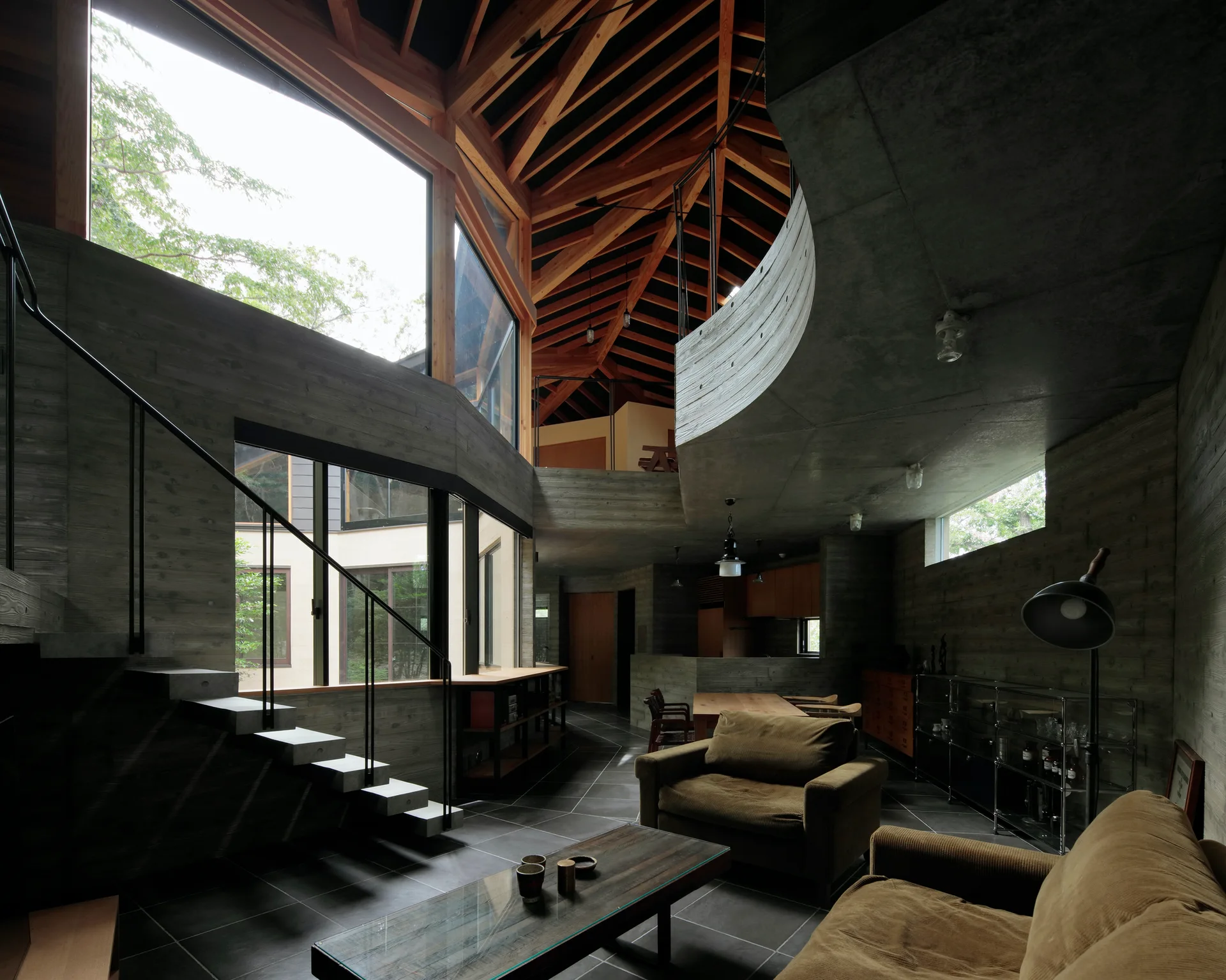 A spacious brutalist living room features board-formed concrete walls, floating steps, and an exposed timber ceiling structure over plush brown sofas.