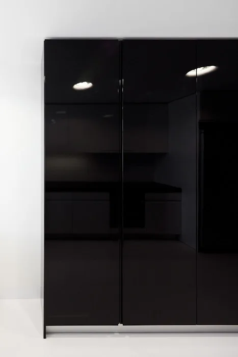 Seamless high-gloss black kitchen cabinets reflecting ambient light beside a minimalist white wall.