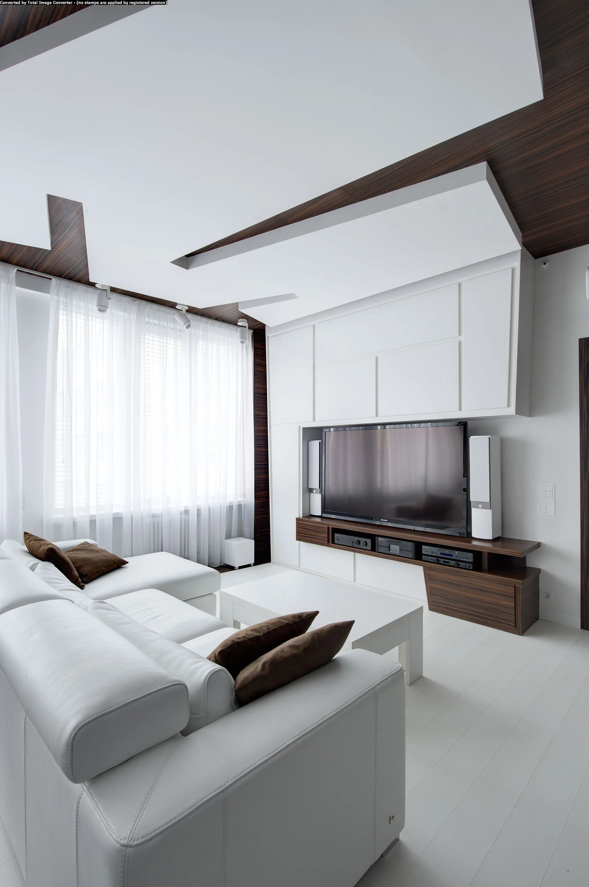 A modern living room features a white leather sectional sofa, a low white coffee table, and a large built-in media console with a television.