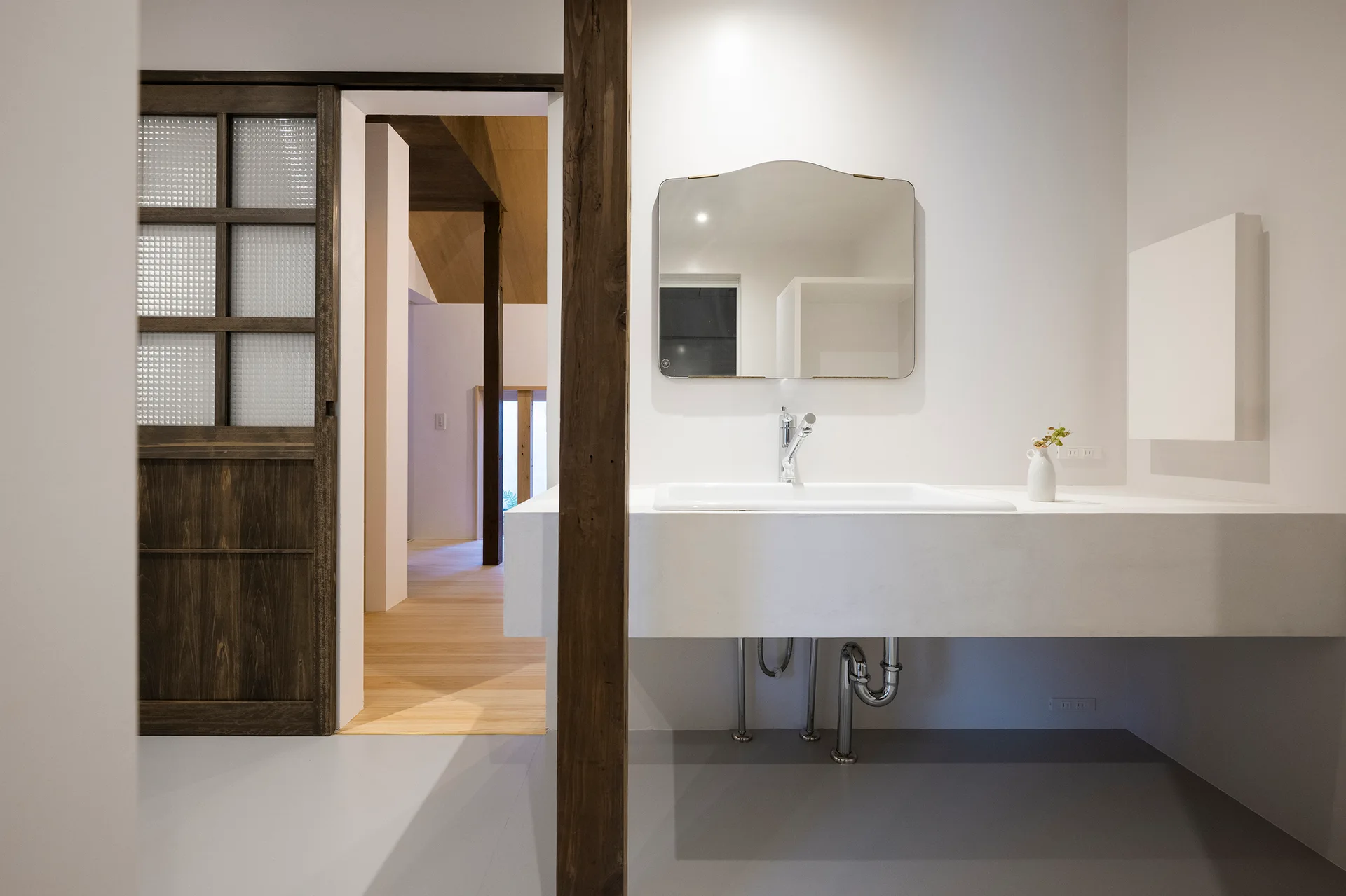 A minimalist bathroom features a floating white sink vanity, a curved rectangular mirror, and a dark wood sliding door with textured glass panels.