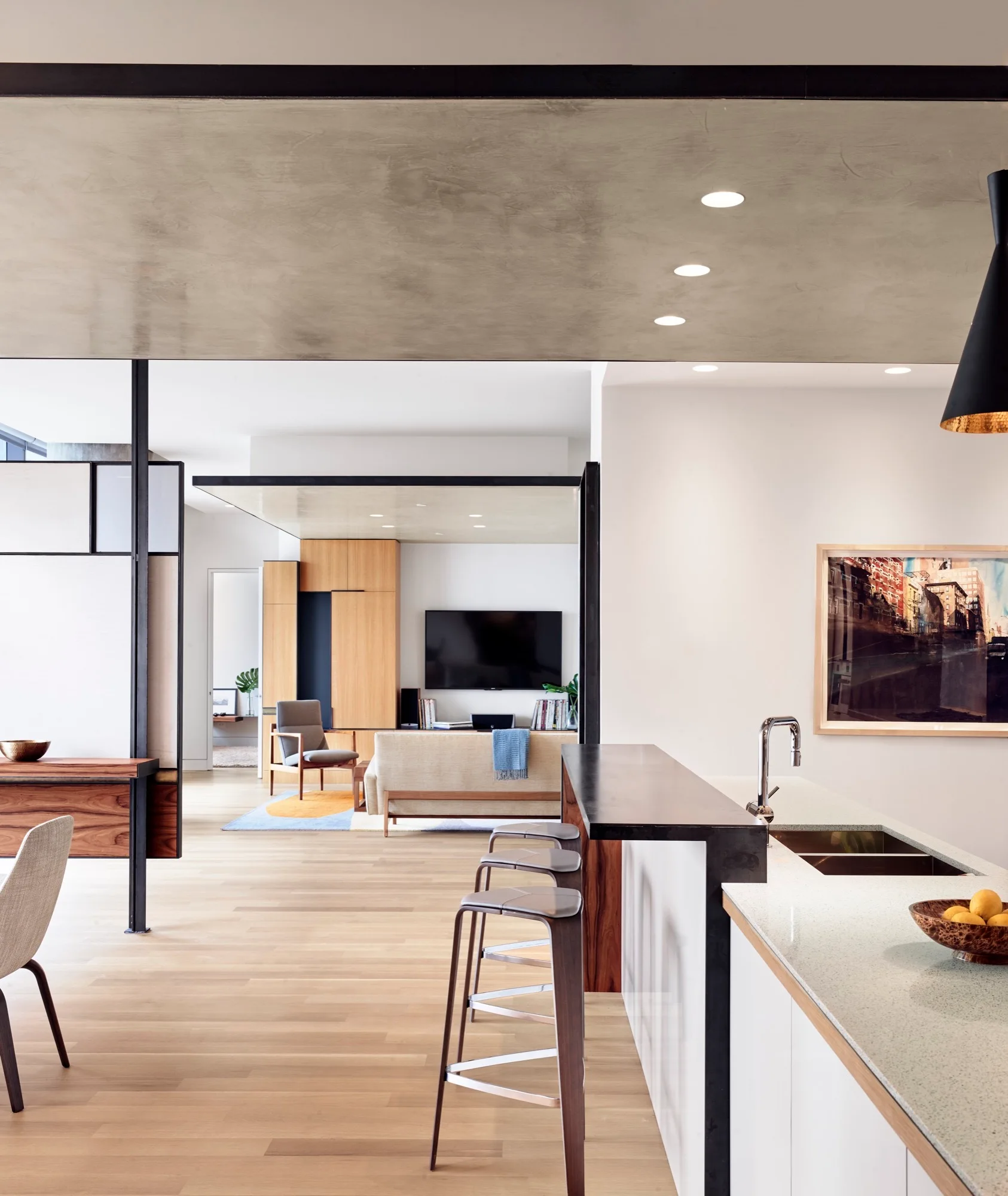 A modern open-concept kitchen with a white island and bar stools, looking toward a living room with a wood media center.