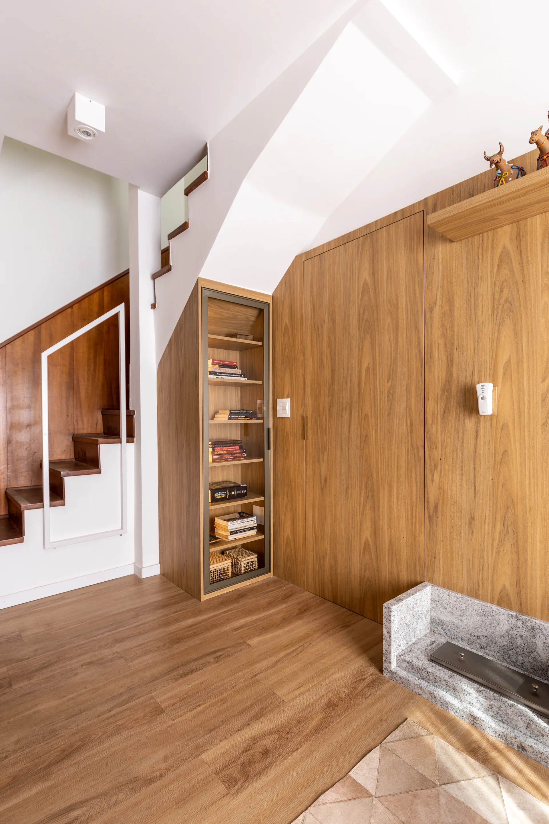 A wooden staircase area featuring integrated wood-toned closets, a built-in glass-door bookcase, and a granite fireplace hearth on wood flooring.