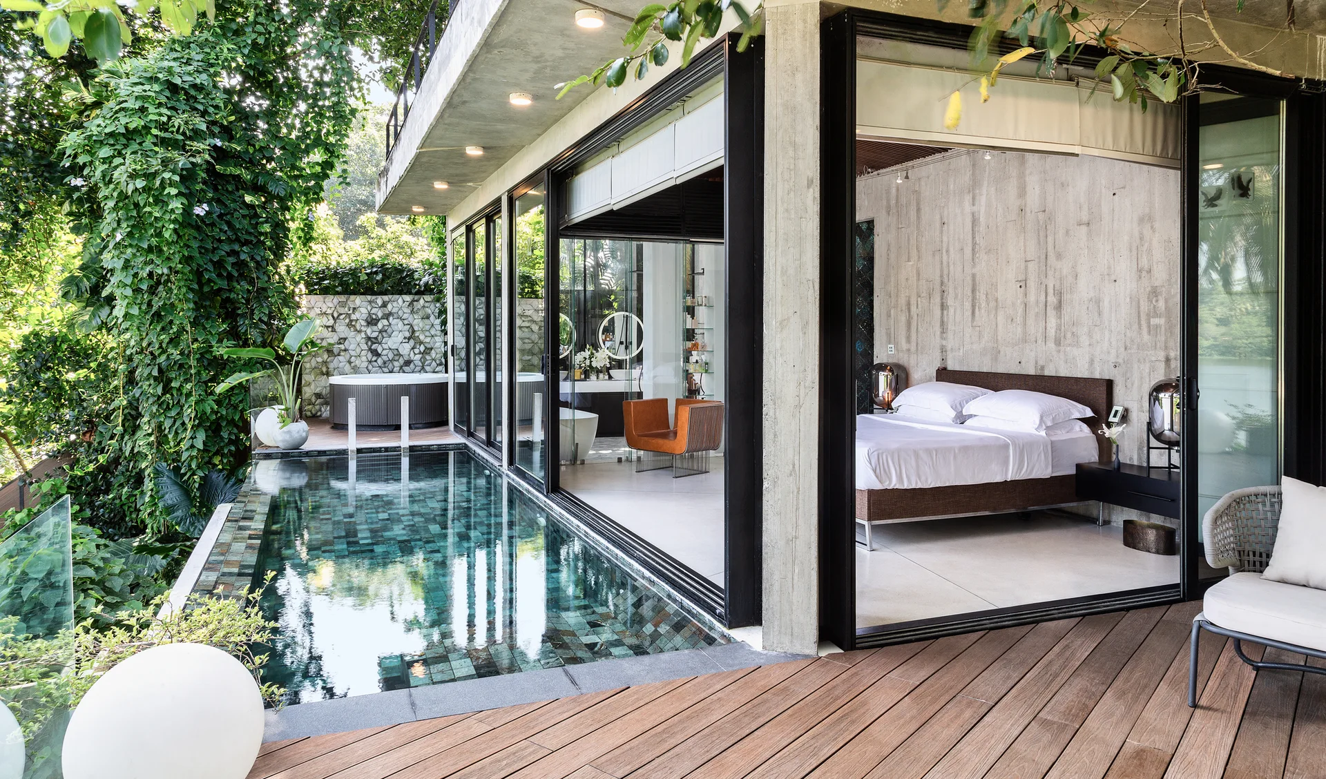 A modern bedroom with concrete walls and large sliding glass doors opening directly onto a patio with a swimming pool.