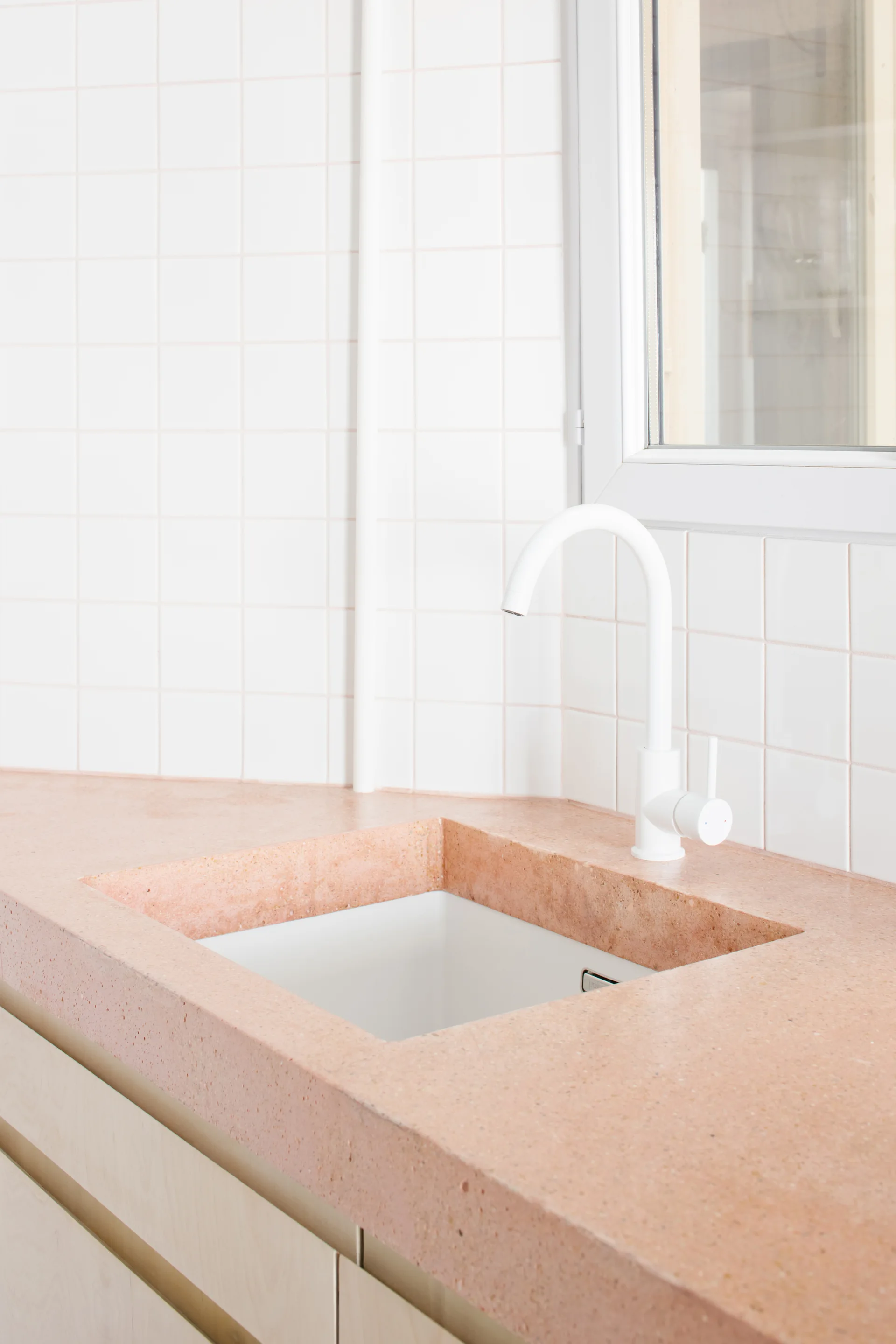 A bathroom vanity features a pink terrazzo countertop, an integrated sink with a white faucet, and a background of white square grid wall tiles.