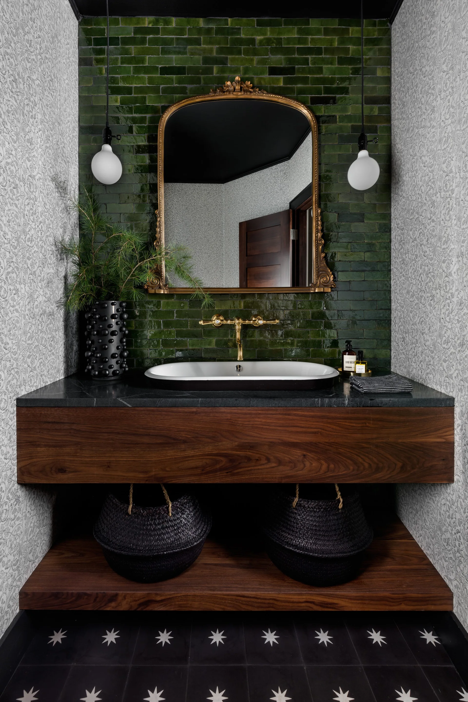 A powder room features a floating walnut vanity with a white vessel sink against a green subway tile wall and an ornate gold mirror.