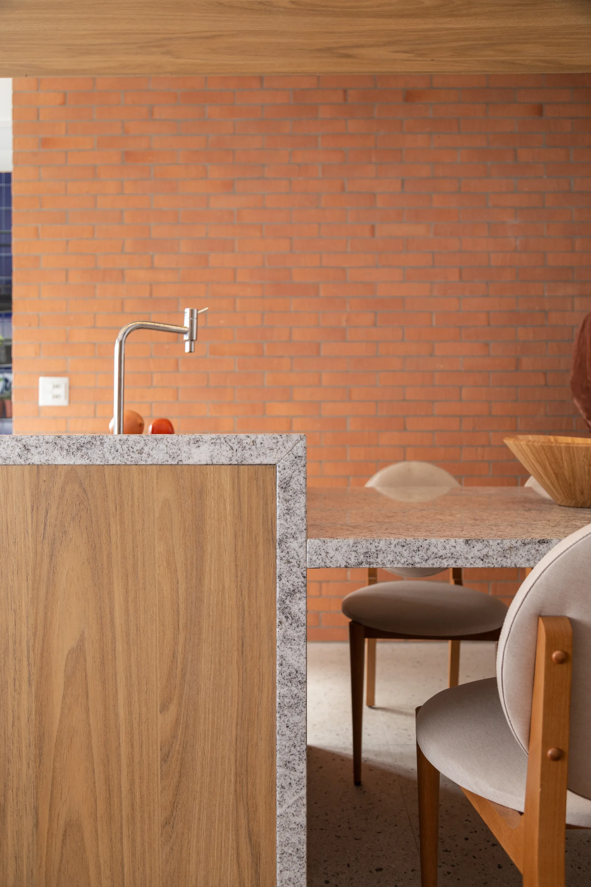 A kitchen island with a speckled stone countertop and wood panels sits adjacent to a matching dining table set against an exposed brick wall.