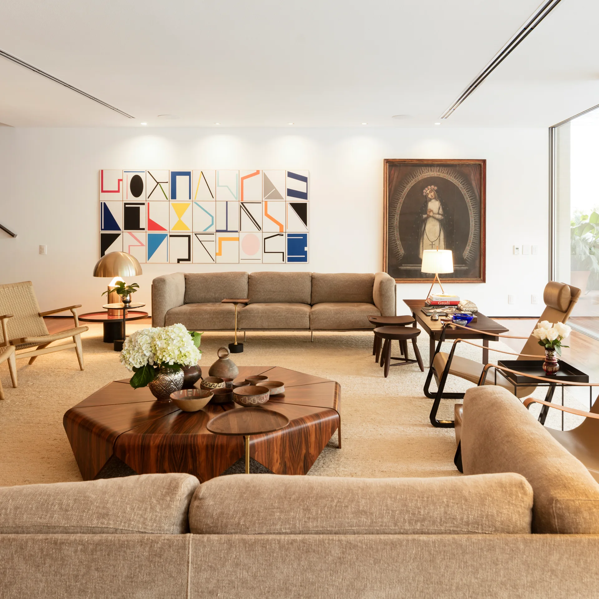 A spacious neutral living room featuring a large beige sofa, a hexagonal wood coffee table, and an eclectic mix of abstract and traditional wall art.