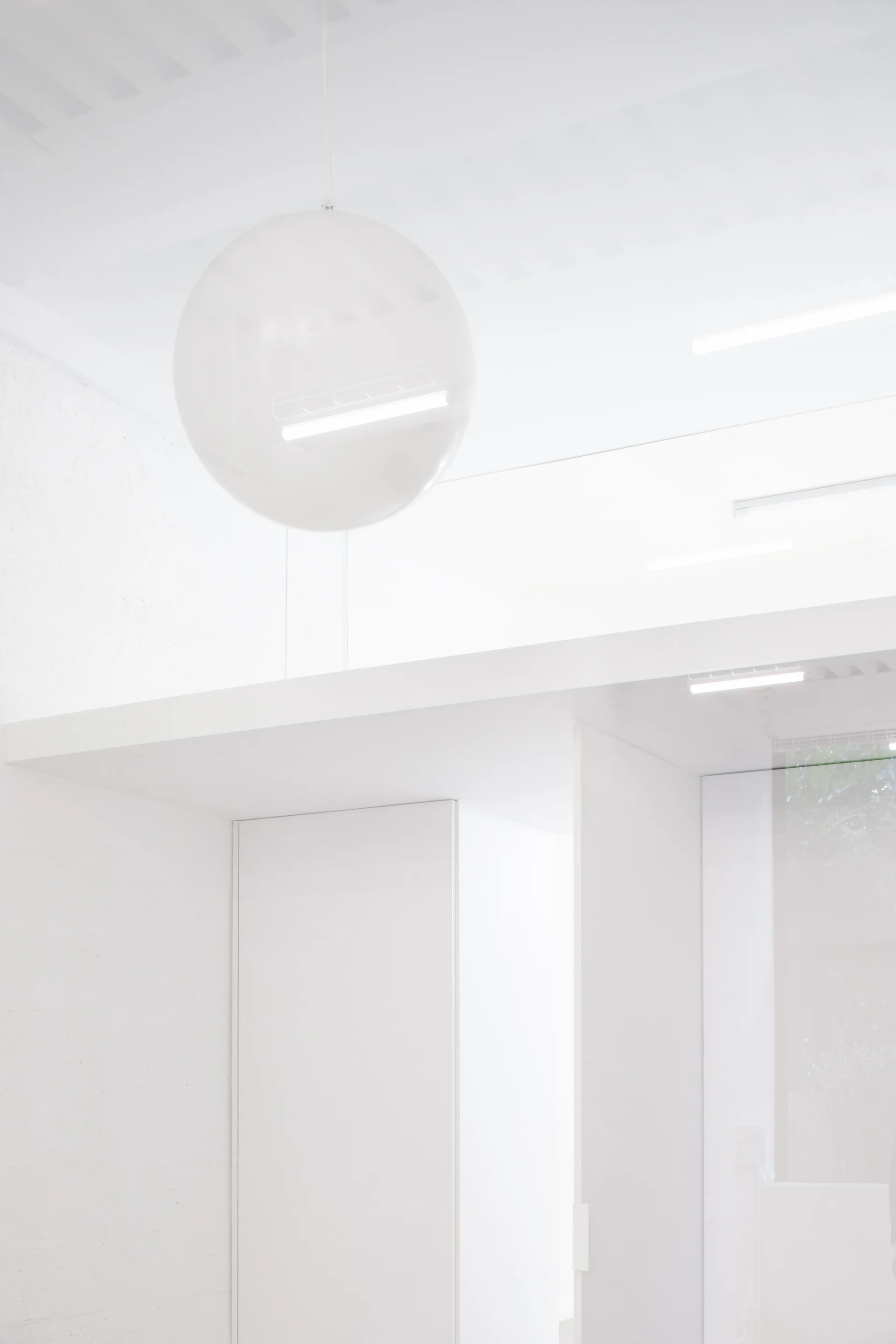 A minimalist white interior features a large spherical pendant light hanging from a white ceiling alongside integrated linear strip lighting.