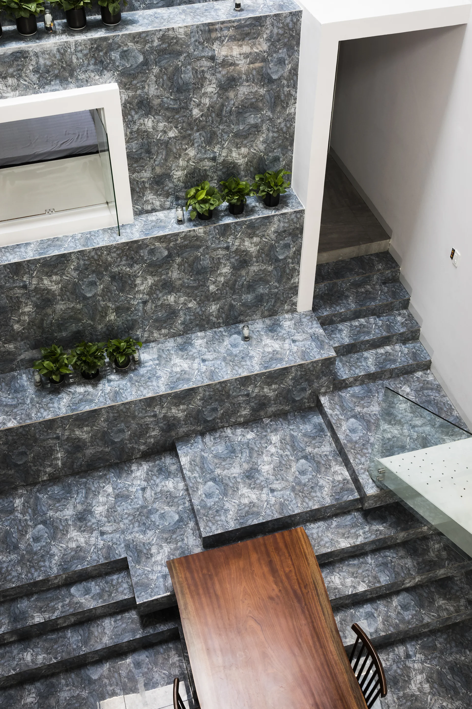A high angle view of a multi level architectural staircase clad in blue mottled stone with integrated ledges holding small green plants.