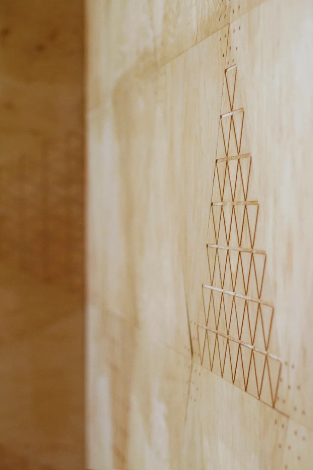 A light tan plywood wall panel features an etched geometric design of stacked triangles.