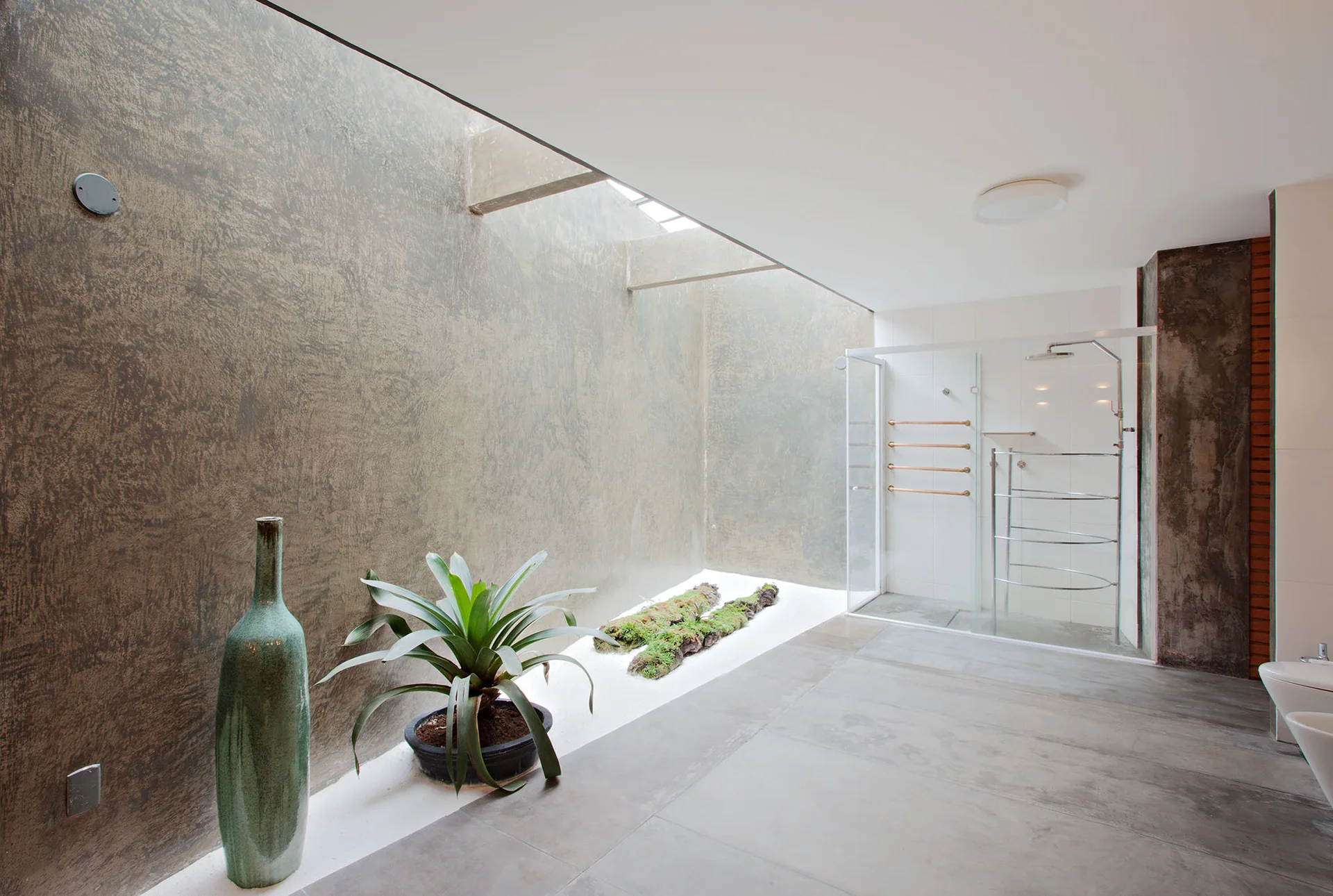 A contemporary minimalist bathroom features a glass walk-in shower, grey concrete walls, and an indoor garden bed under a skylight.