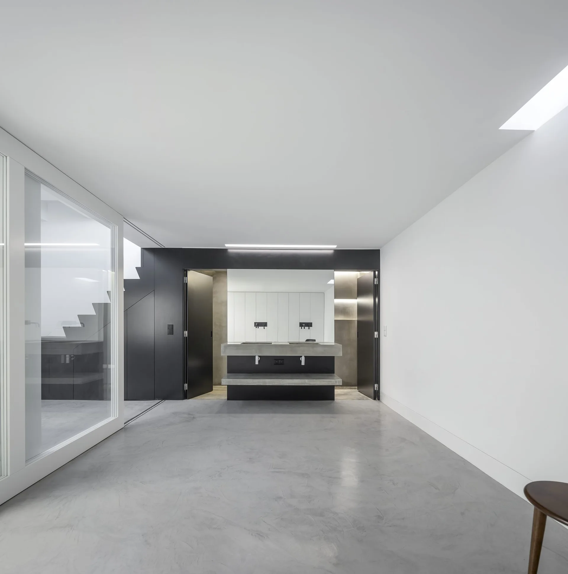 A minimalist bathroom featuring a floating concrete vanity under a large mirror, flanked by black doors on a polished gray concrete floor.