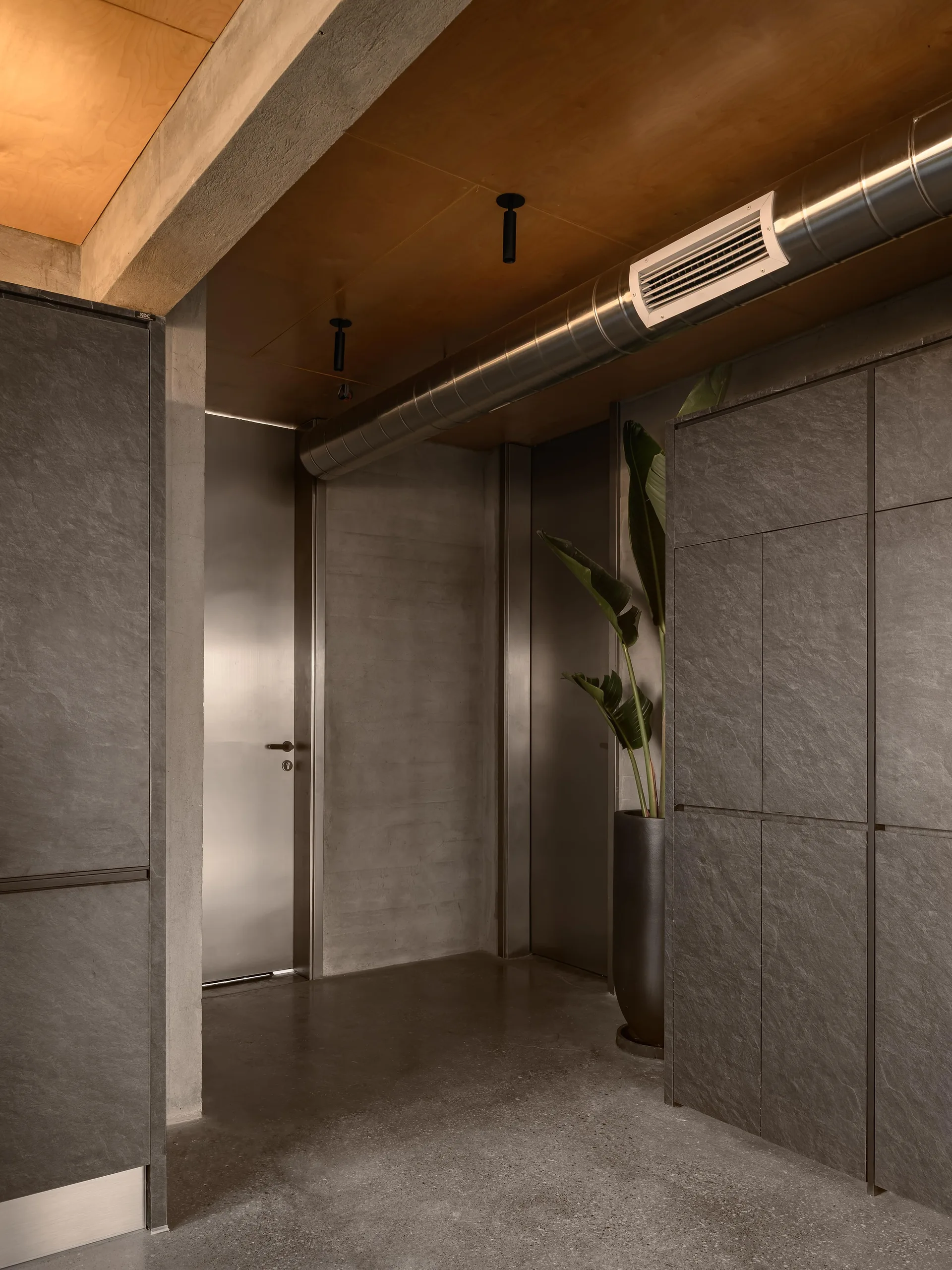 A modern industrial corridor features dark grey slate-textured cabinets, a brushed metal door, and an exposed steel ventilation duct.