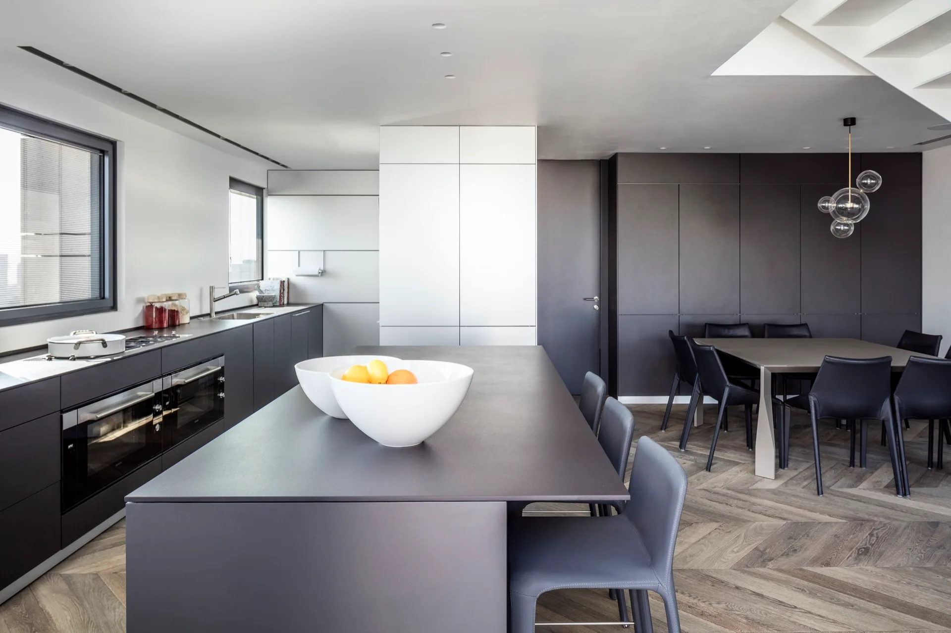 A modern charcoal grey kitchen and dining area with matte cabinets, a central island, and herringbone wood flooring.