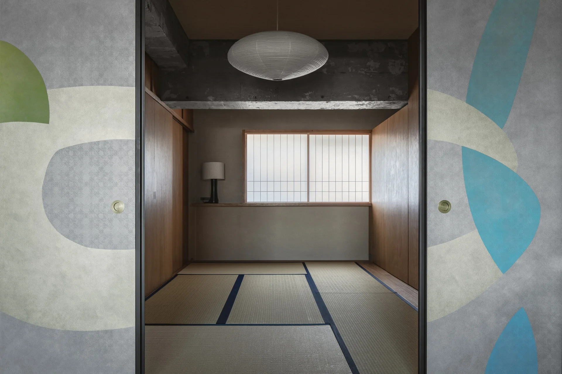 A minimalist Japanese bedroom seen through sliding doors with abstract patterns, featuring tatami mats and an exposed concrete ceiling beam.
