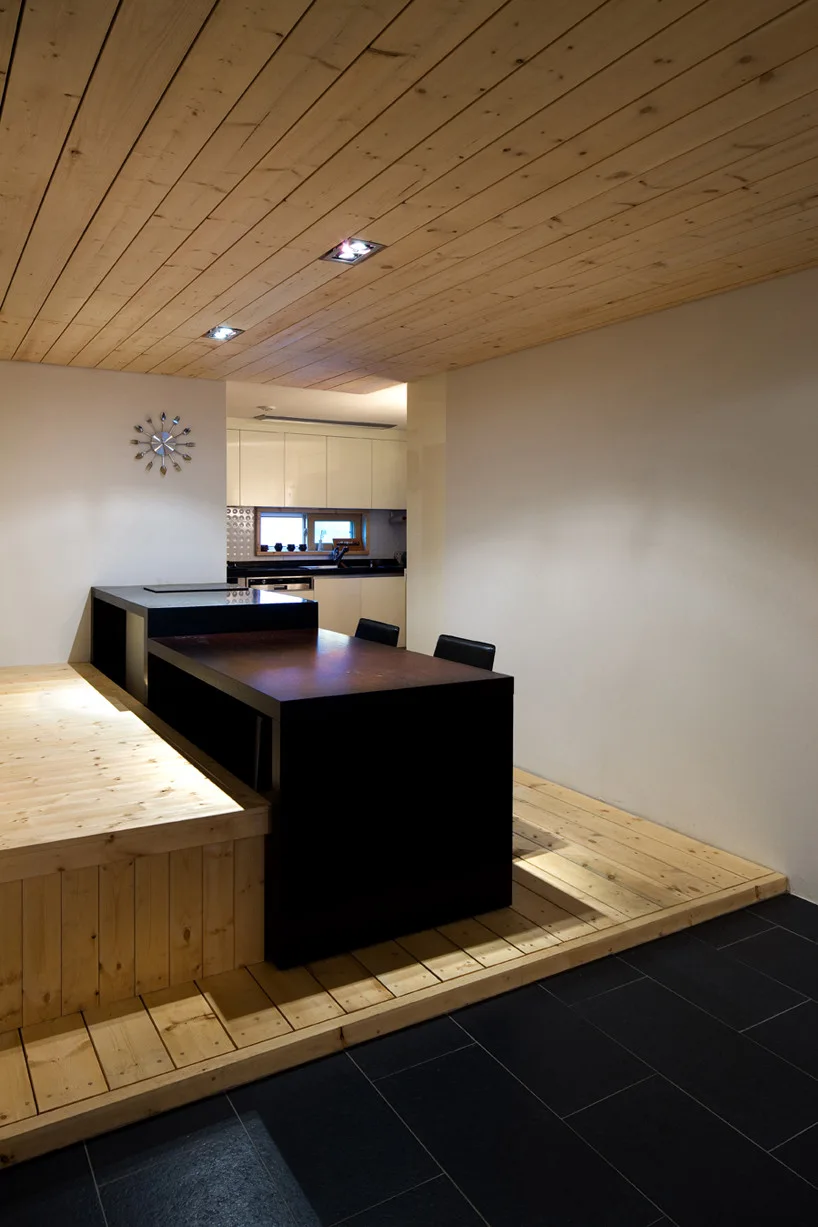 A kitchen dining space featuring a raised light wood platform, a dark wood island table, and a matching light wood planked ceiling.
