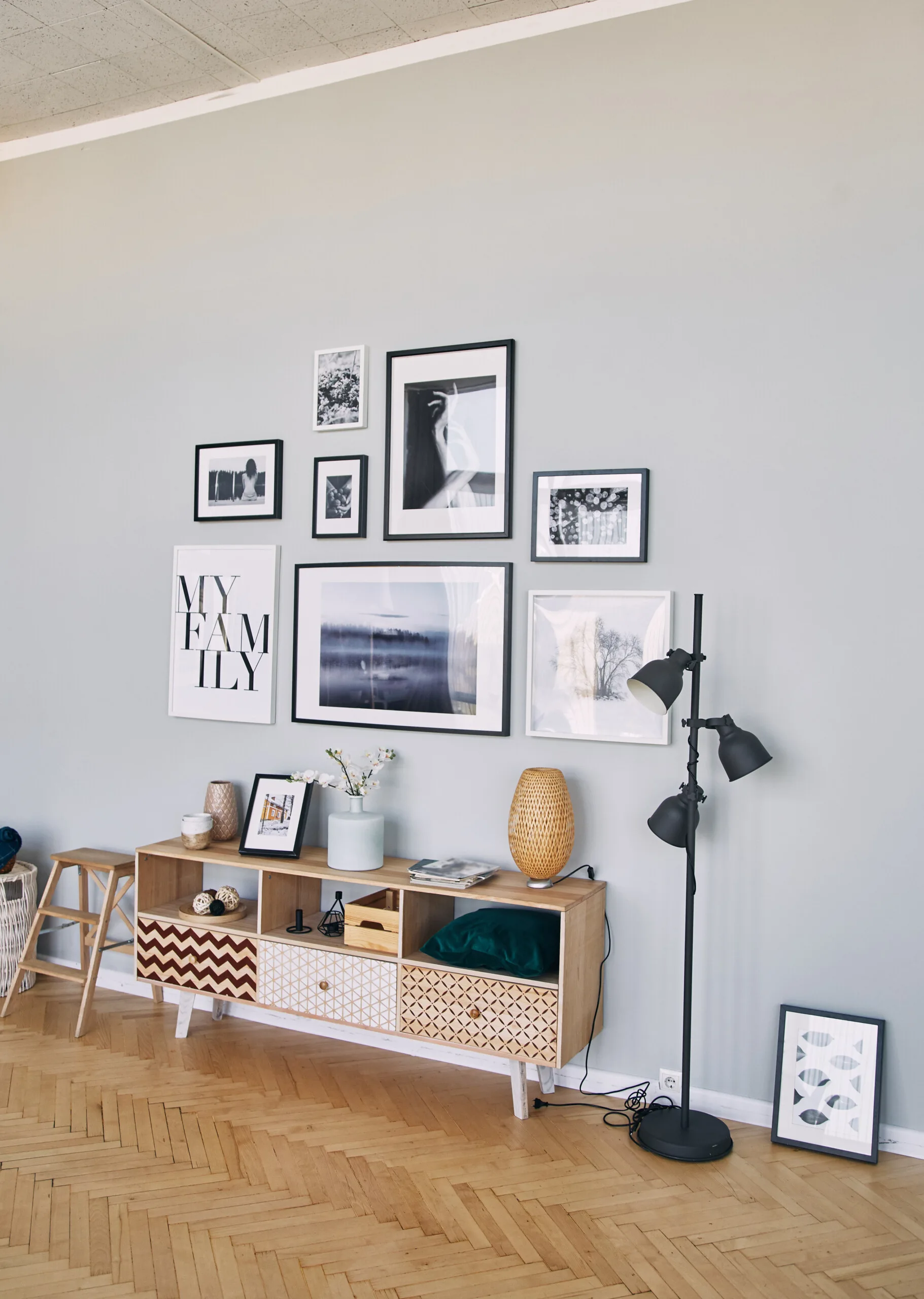 A gallery wall of black and white framed photos hangs on a light blue wall above a patterned wooden console table on herringbone wood floors.