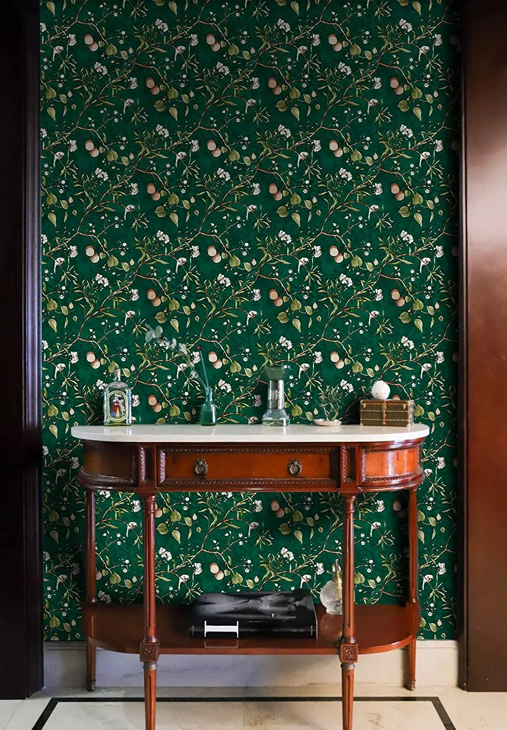 A curved wooden console table with a polished marble top sits in a niche framed by dark wood trim and backed by dark green botanical wallpaper.