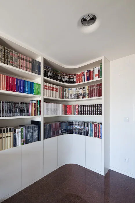 A custom white corner bookshelf with a curved inner design is filled with books above dark polished floor tiles.