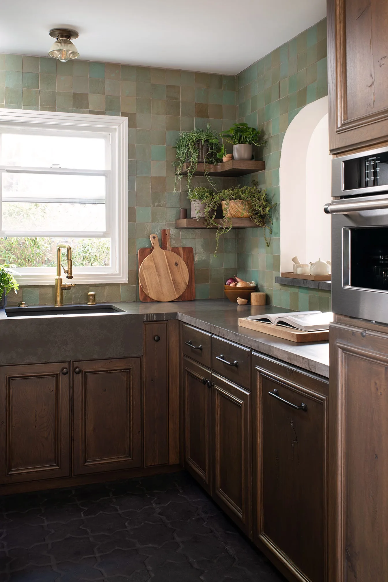 A kitchen corner features dark wood cabinets, a dark apron-front sink with a brass faucet, and walls covered in green square tiles.