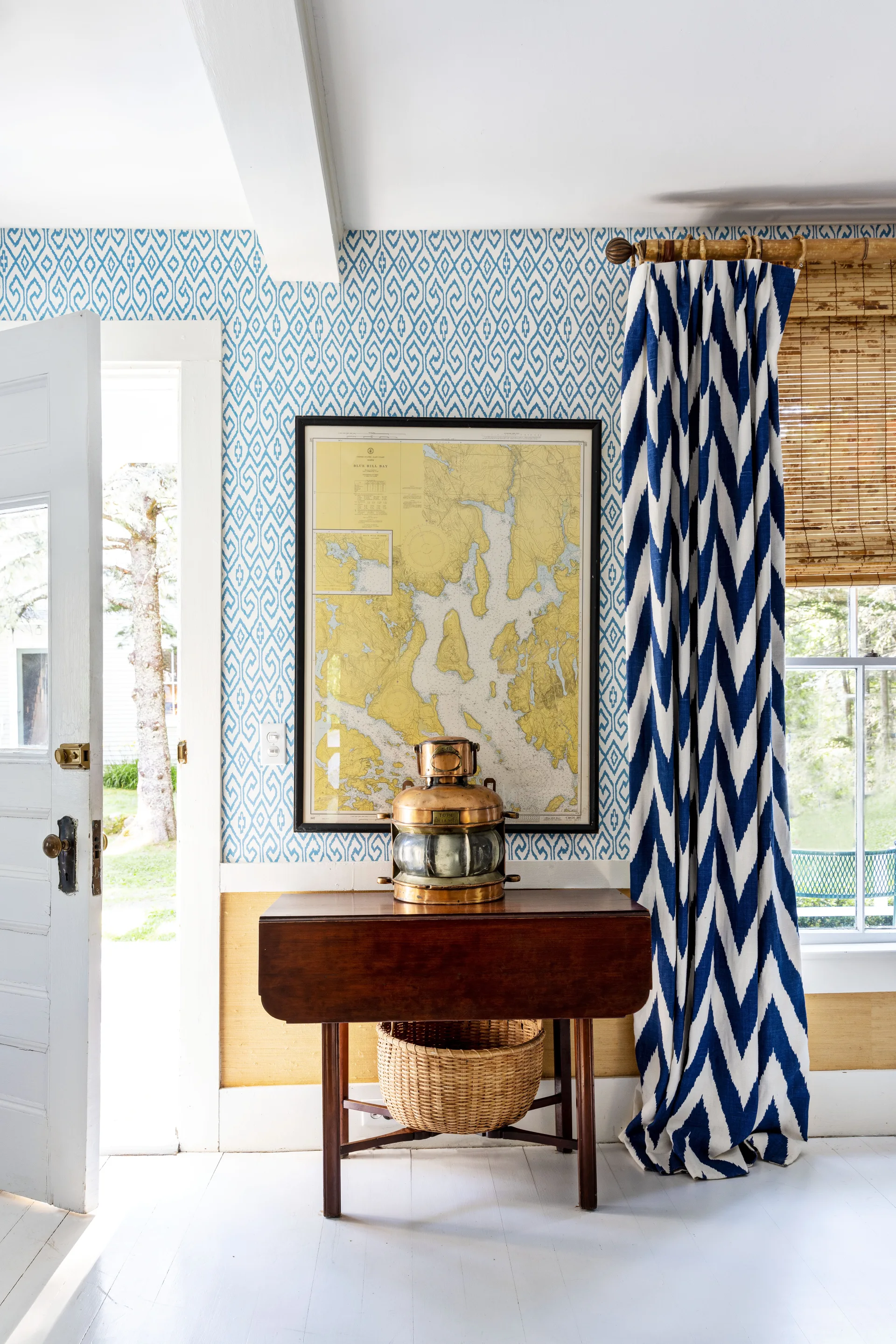 A bright entryway features a wooden drop-leaf table with a brass lantern, set against blue geometric wallpaper and a framed map.