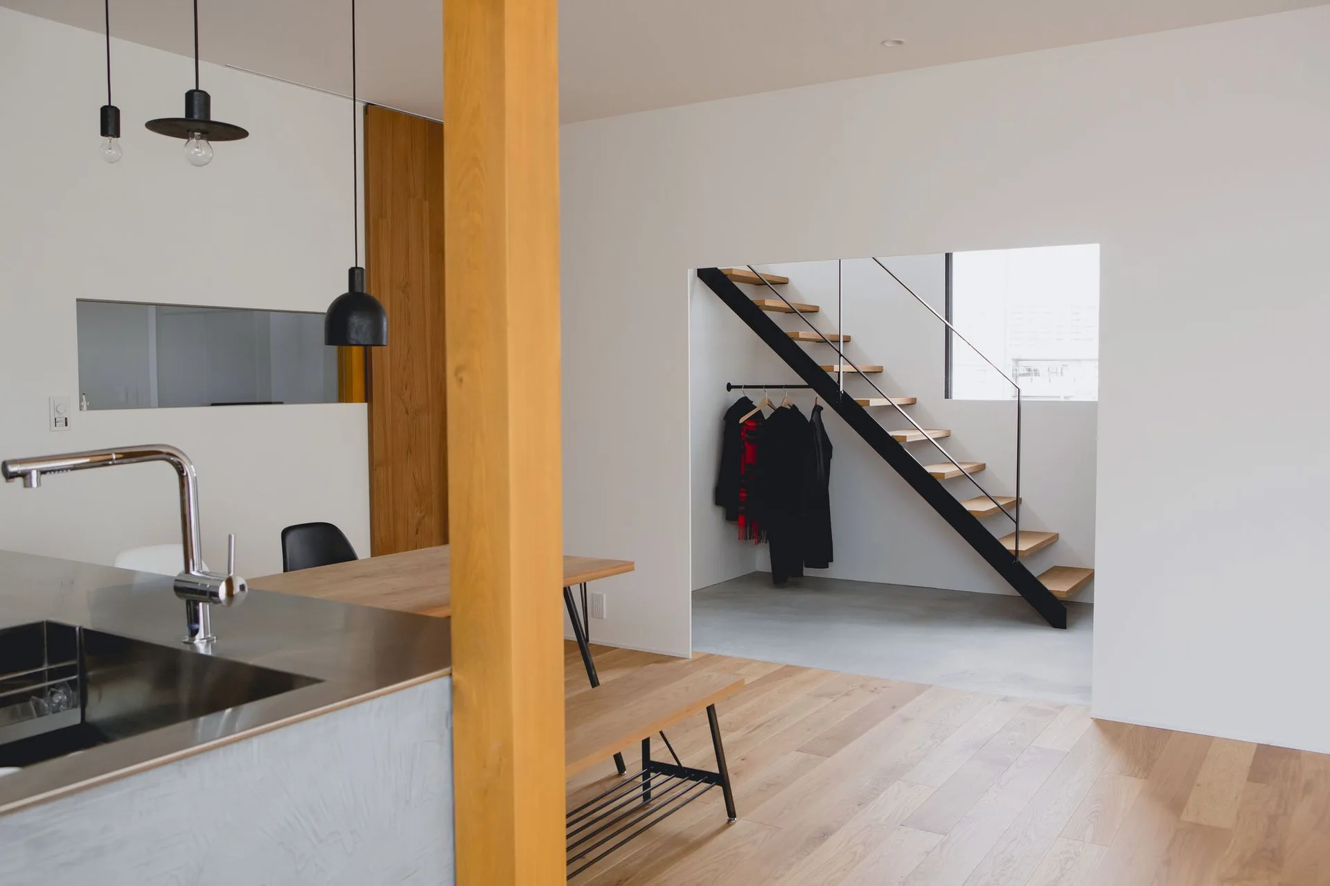 A minimalist kitchen with a stainless steel sink features a wooden dining table and an open riser staircase in the background.