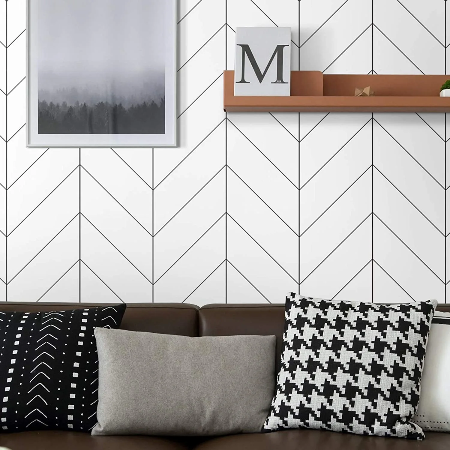 A brown leather sofa sits against a wall styled with black and white herringbone wallpaper, a floating terracotta shelf, and framed art.