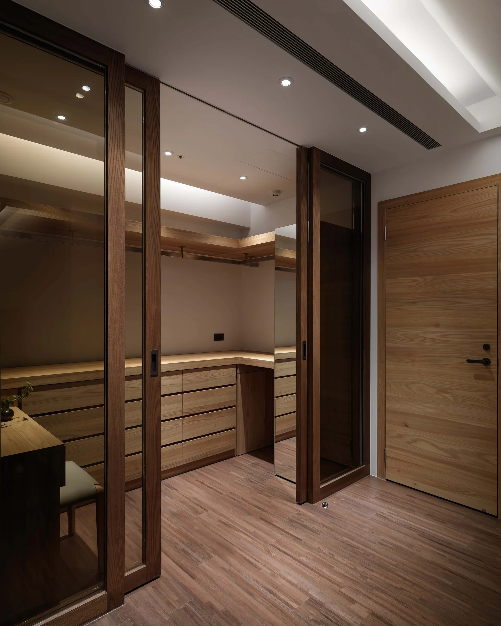 A modern walk-in closet featuring built-in wood cabinetry, drawers, integrated mirror panels, and wood-framed glass sliding doors.